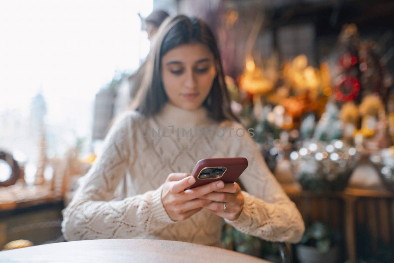 A lovely, radiant girl capturing moments in the Christmas decor store with her smartphone. High quality photo