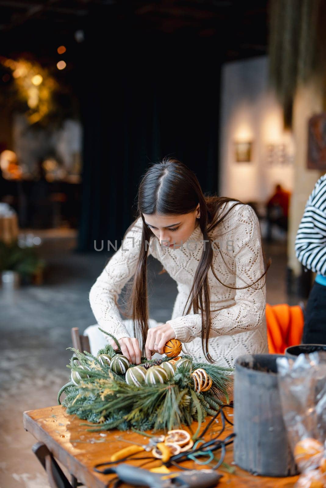 An elegant young woman passionately learning at a Christmas decor workshop. by teksomolika