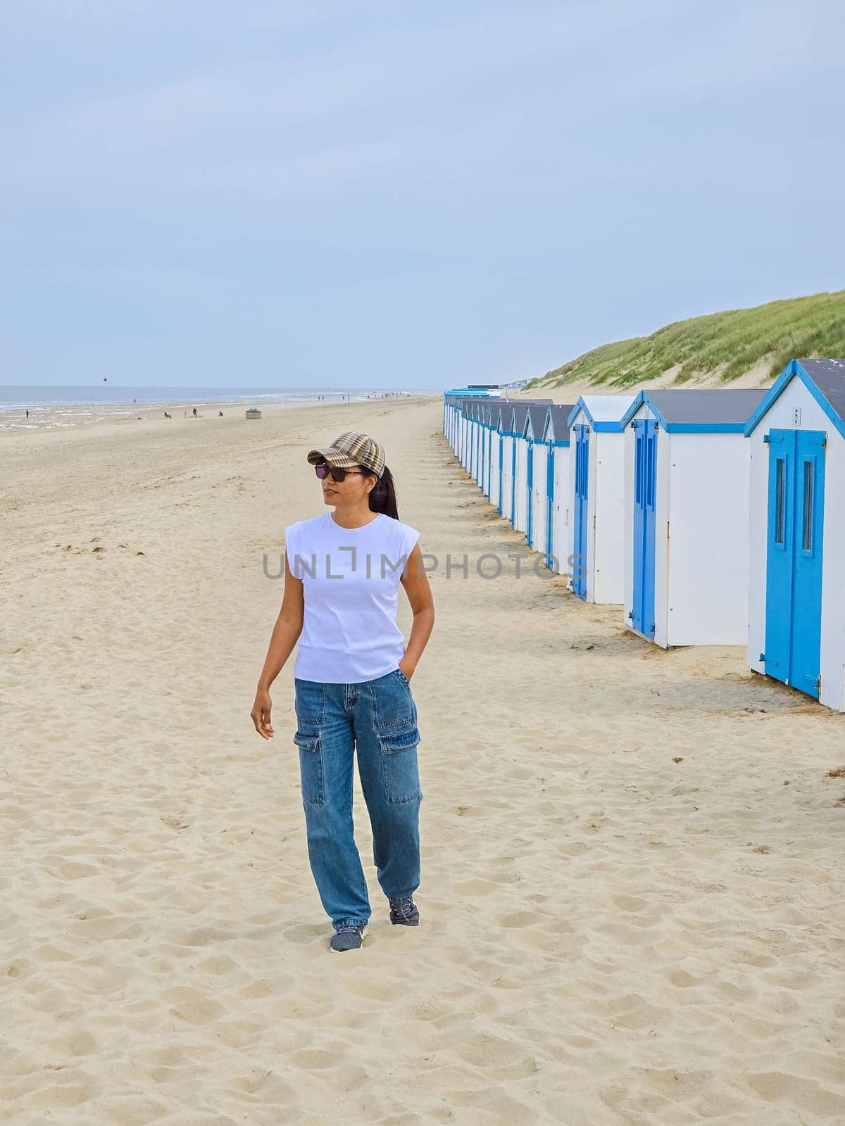 A stylish woman strolls gracefully, passing by a vibrant row of beach huts lining the Texel, Netherlands coastline.