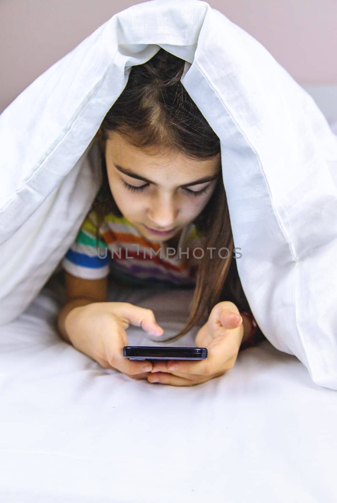 The child plays with the phone in bed. Selective focus. Kid.