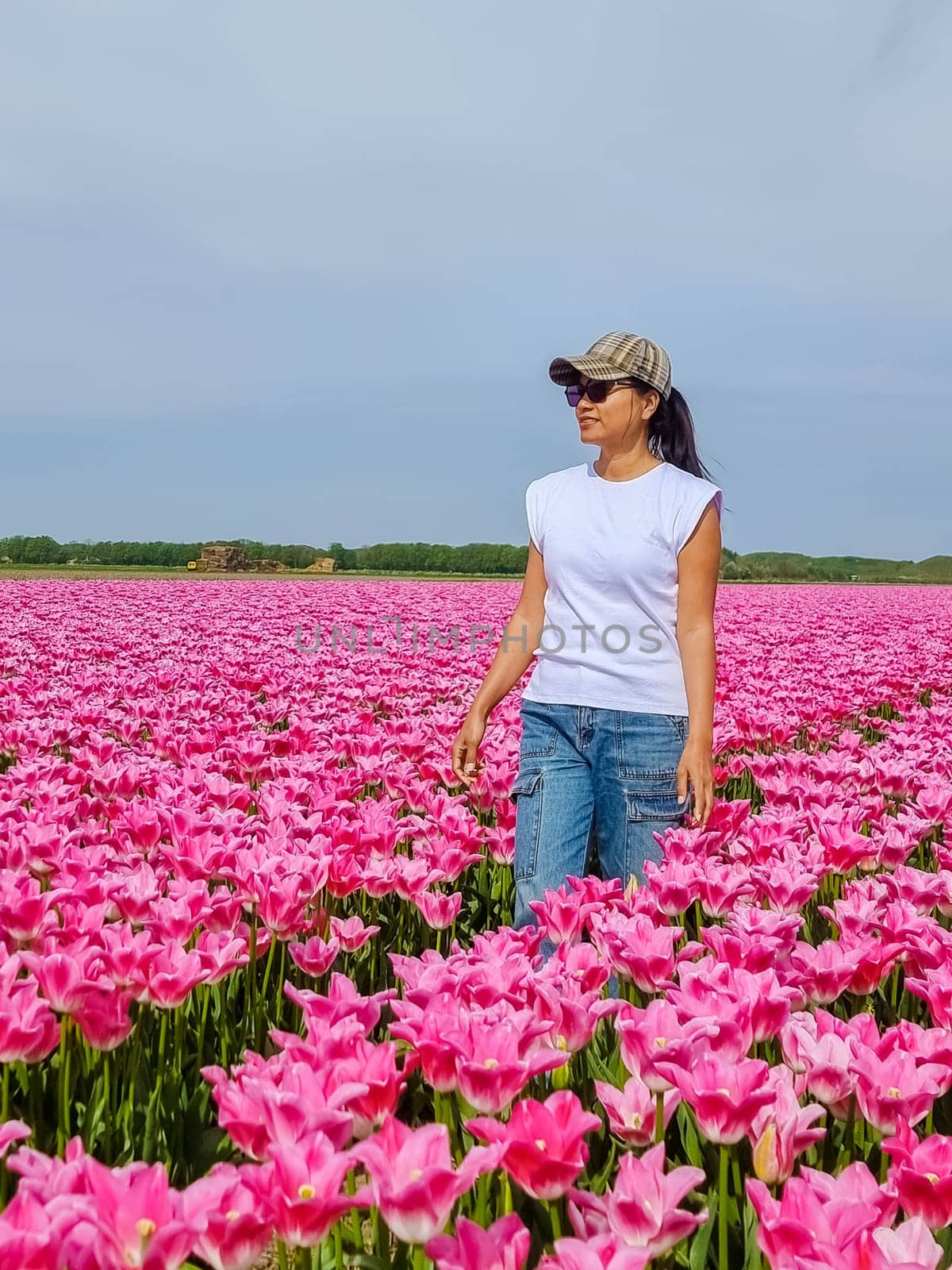 A woman stands elegantly in a field of vibrant pink tulips, surrounded by their beauty and serenity.