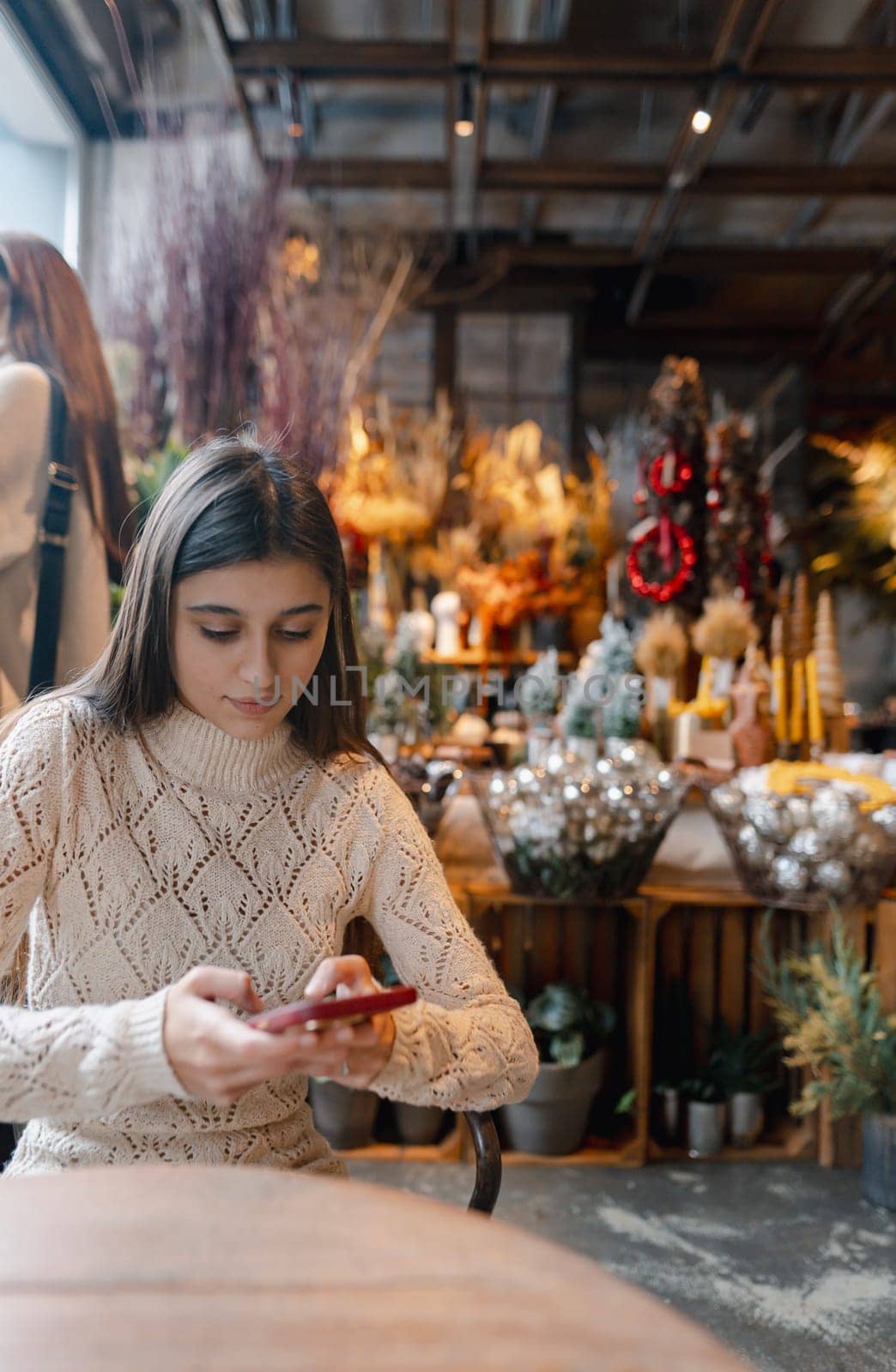 A gorgeous, bright young lady exploring holiday decorations while holding her smartphone. by teksomolika