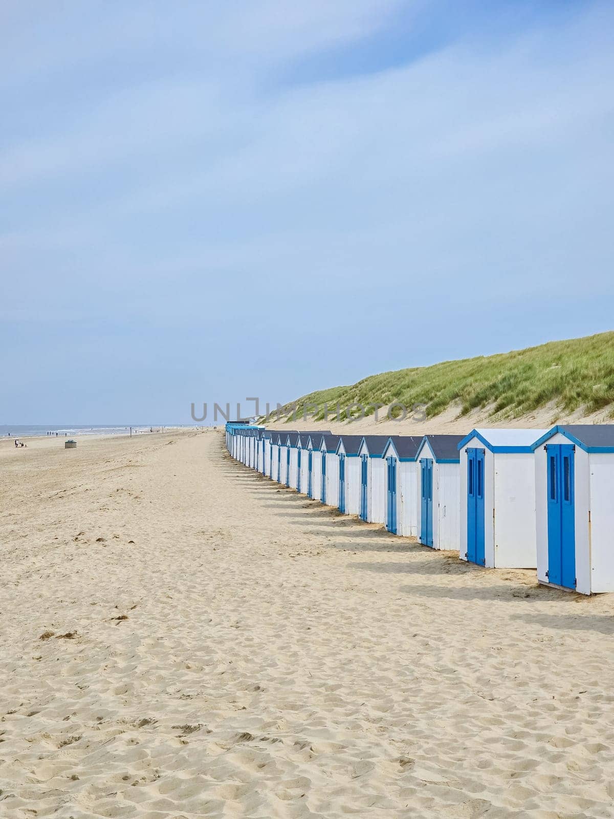 A vibrant row of beach huts line the sandy beach under a clear blue sky, adding a splash of color to the serene seascape.