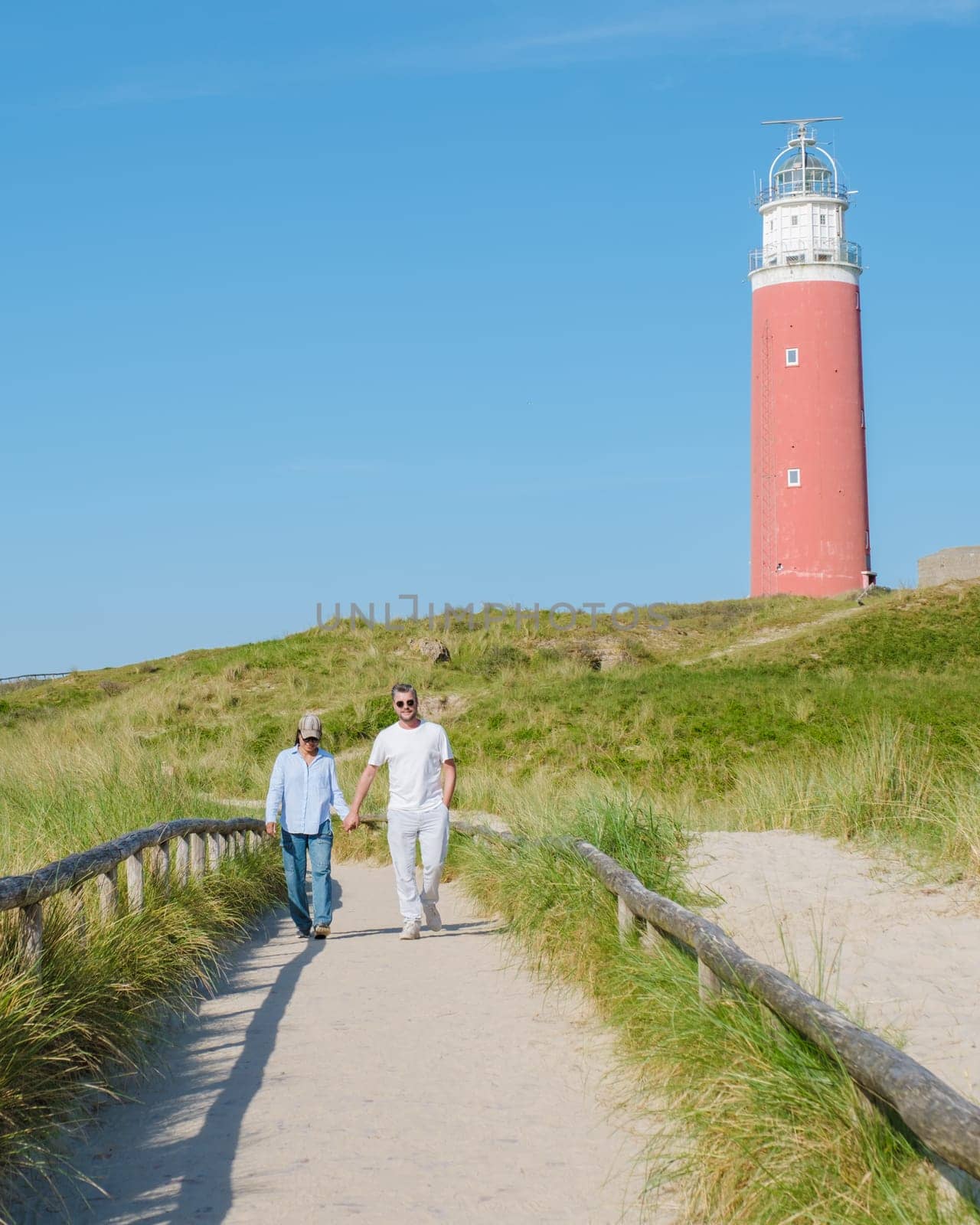 A couple strolling along a path by a stunning lighthouse in Texel, Netherlands, enjoying the scenic view and the peaceful surroundings.