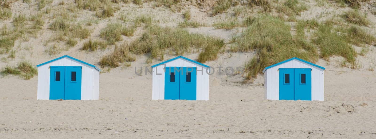 Four colorful beach huts stand in a row on the sandy shore of Texel, Netherlands, under the bright sun.