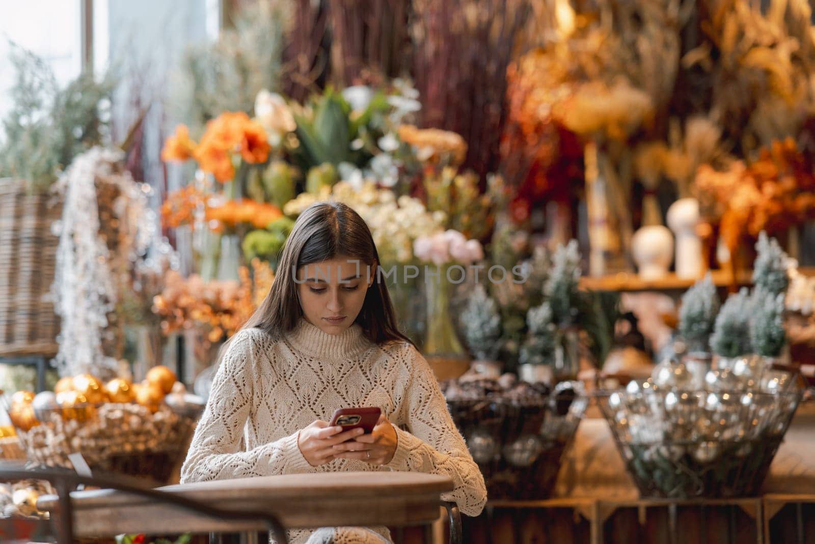 A dazzling, vibrant young woman shopping for New Year's decor and checking her smartphone. by teksomolika