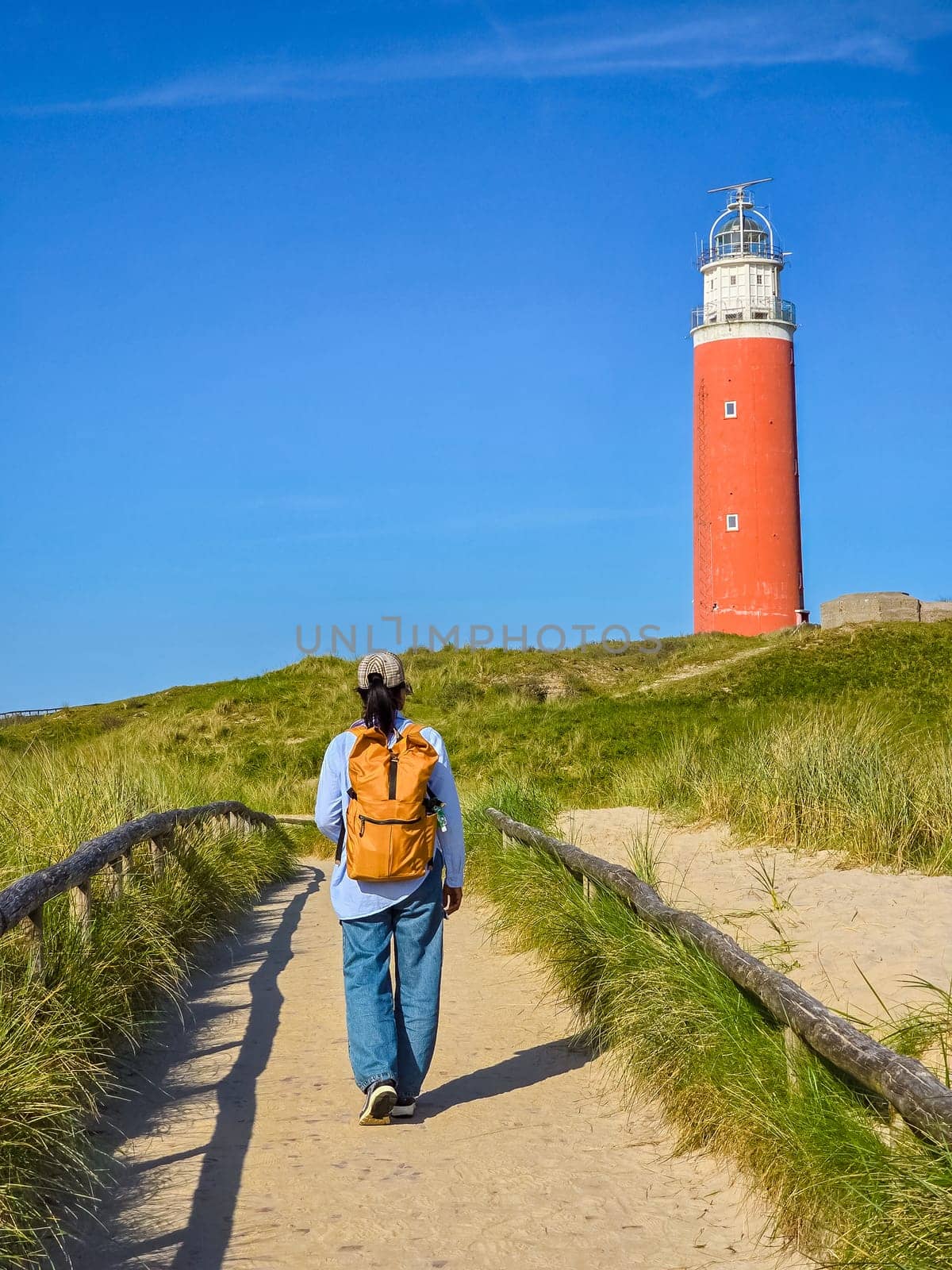 A man walking down a path with a majestic lighthouse standing tall in the background, guiding his way through the Texel, Netherlands.