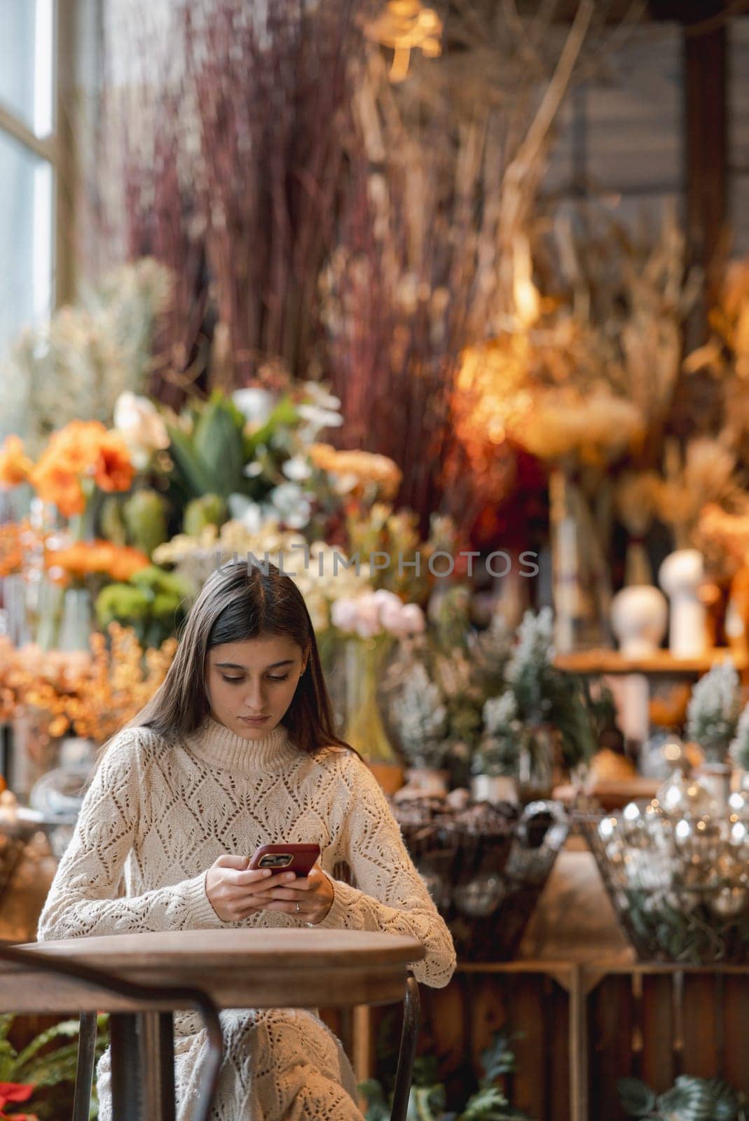 An elegant, bright girl browsing through Christmas decor while using her smartphone. by teksomolika