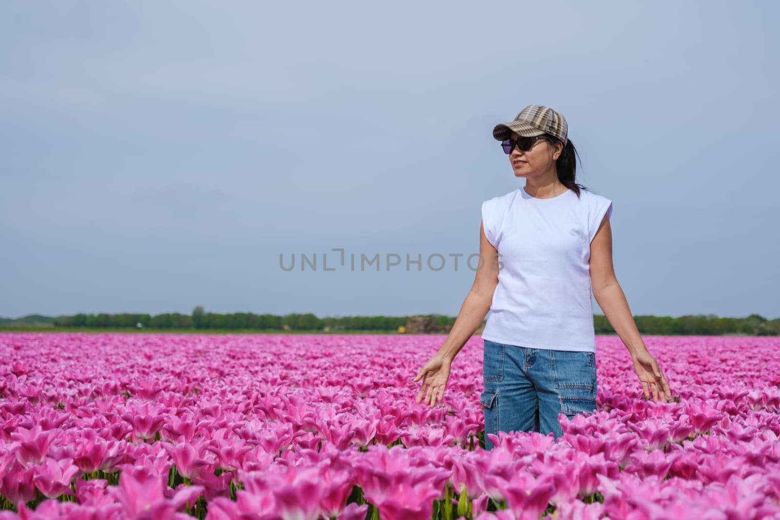 A woman stands gracefully amid a sea of vibrant pink tulips in the scenic Texel, Netherlands, connecting with the beauty of nature by fokkebok