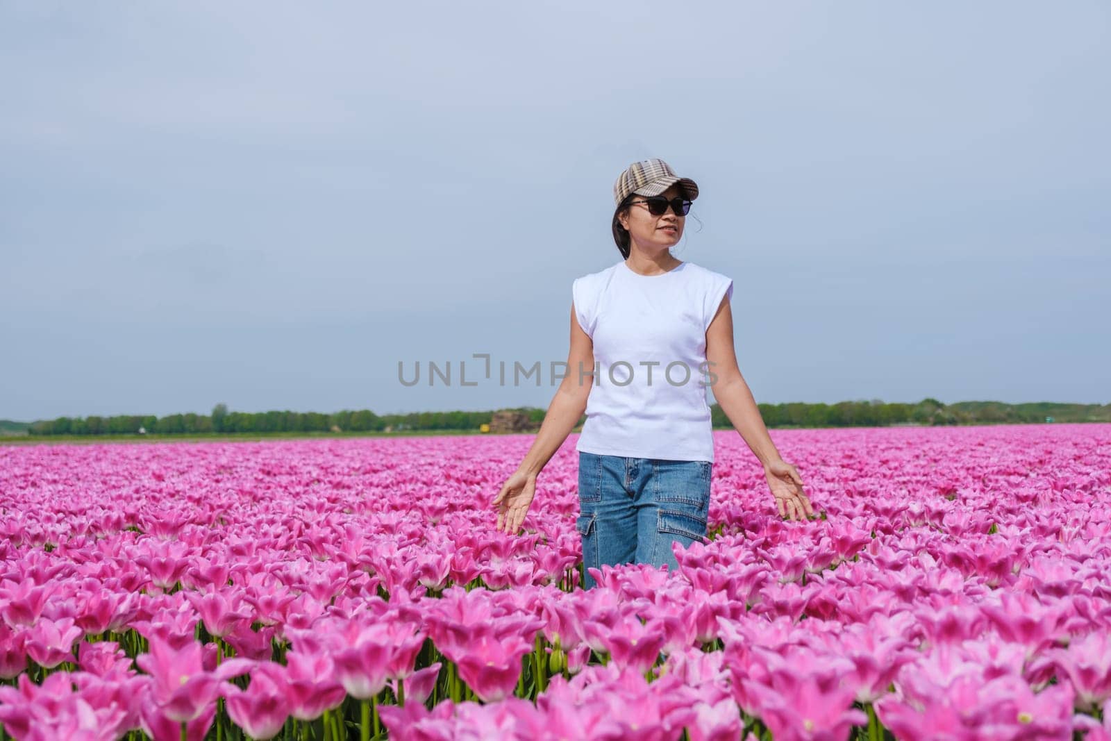 A woman elegantly stands amidst a vibrant sea of pink tulips in a field in Texel, Netherlands by fokkebok