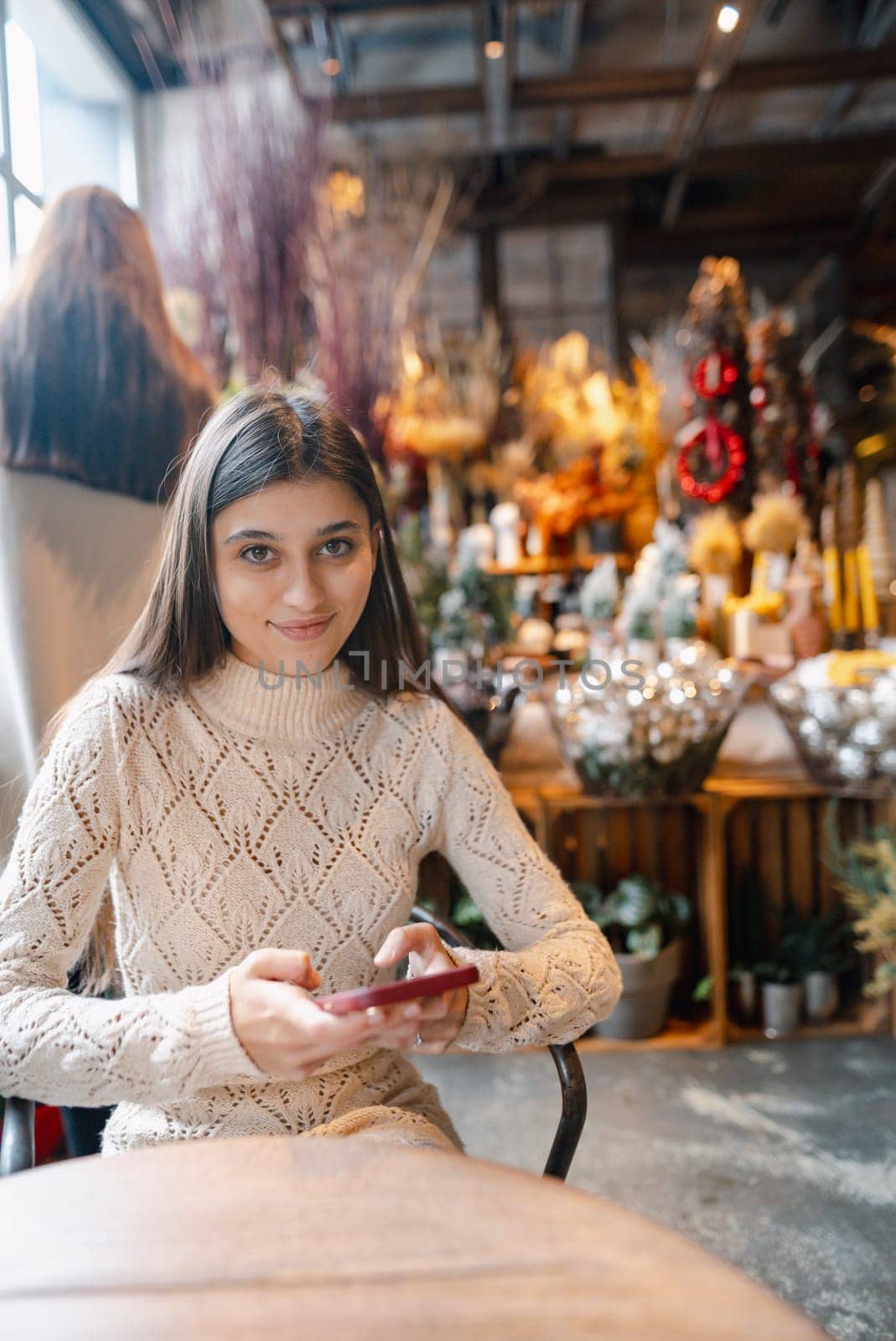A beautiful, vibrant girl with a smartphone in hand at the Christmas decor store. High quality photo