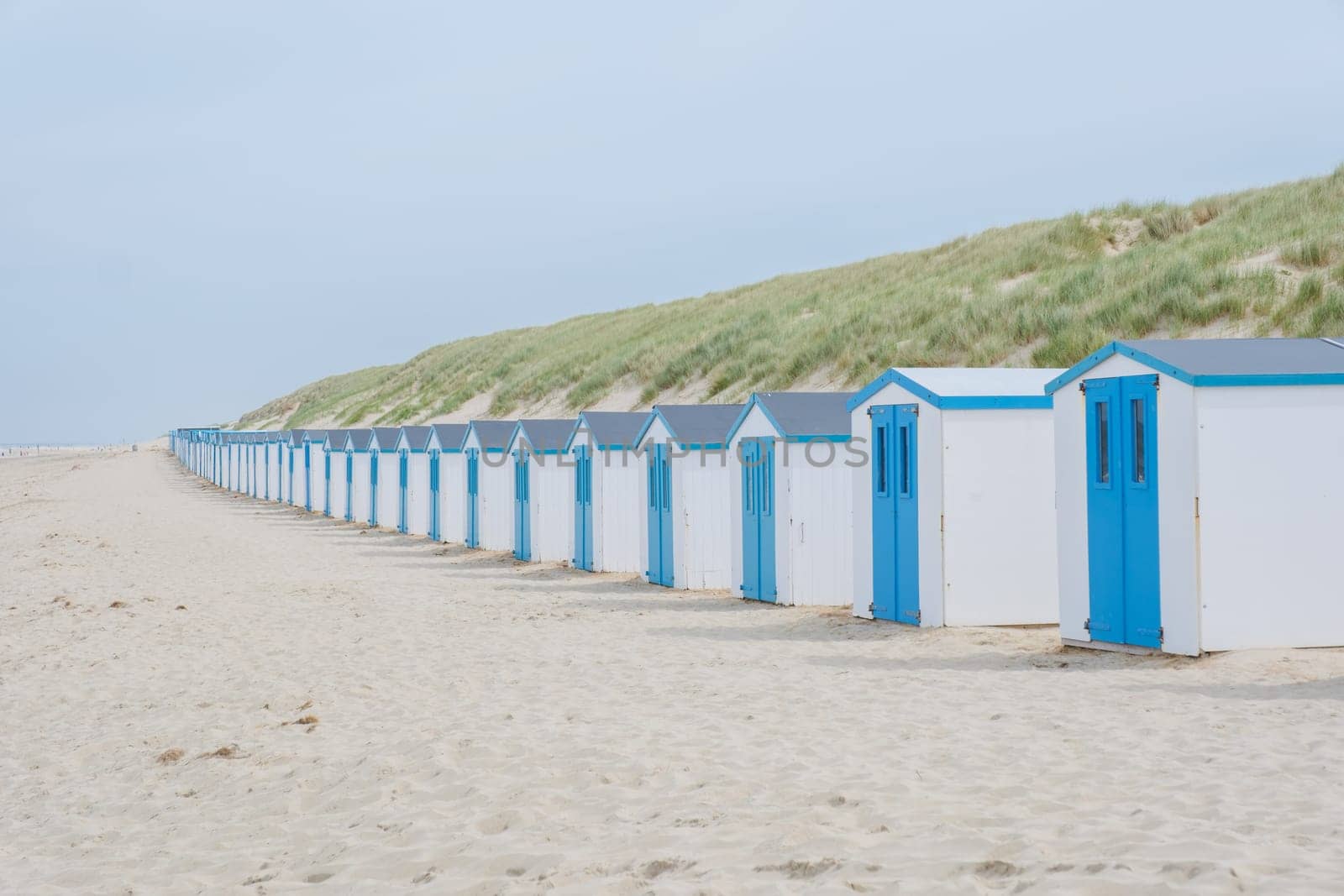 A peaceful scene unfolds as a row of charming blue beach huts stand tall against the sandy backdrop of Texel, Netherlands. De Koog beach Texel