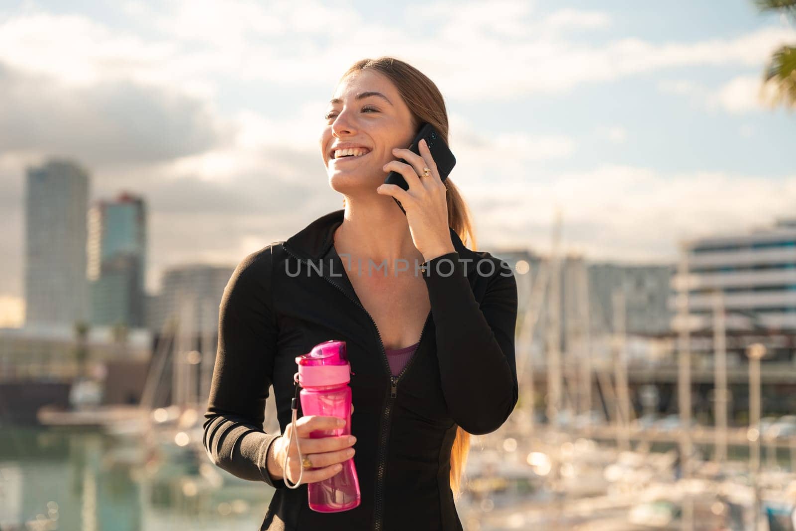 cheerful young woman talking on smartphone and holding sport bottle.