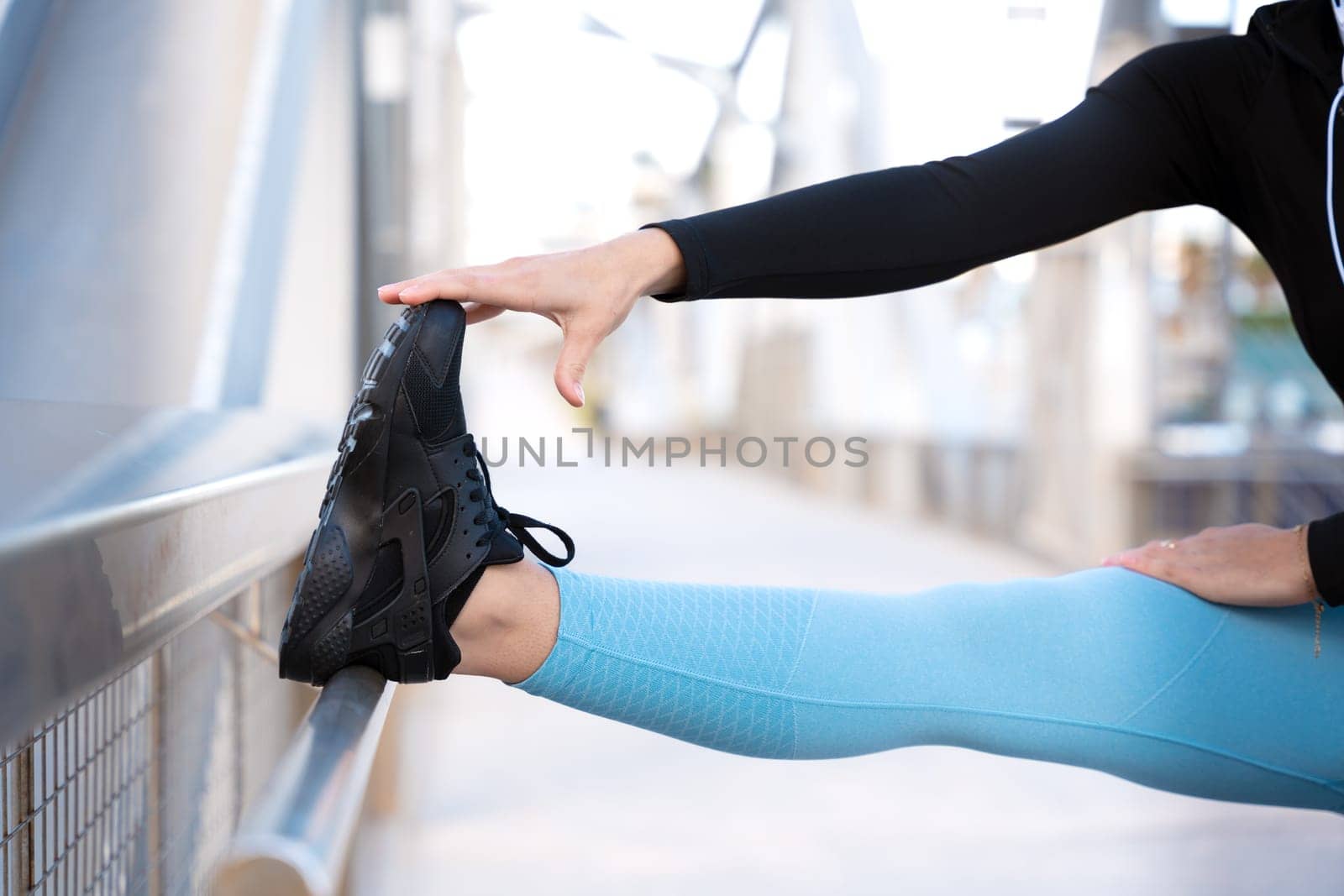 Young sportswoman in sports headphones doing stretching smiling looking at camera with bottle of water on the floor outdoors.