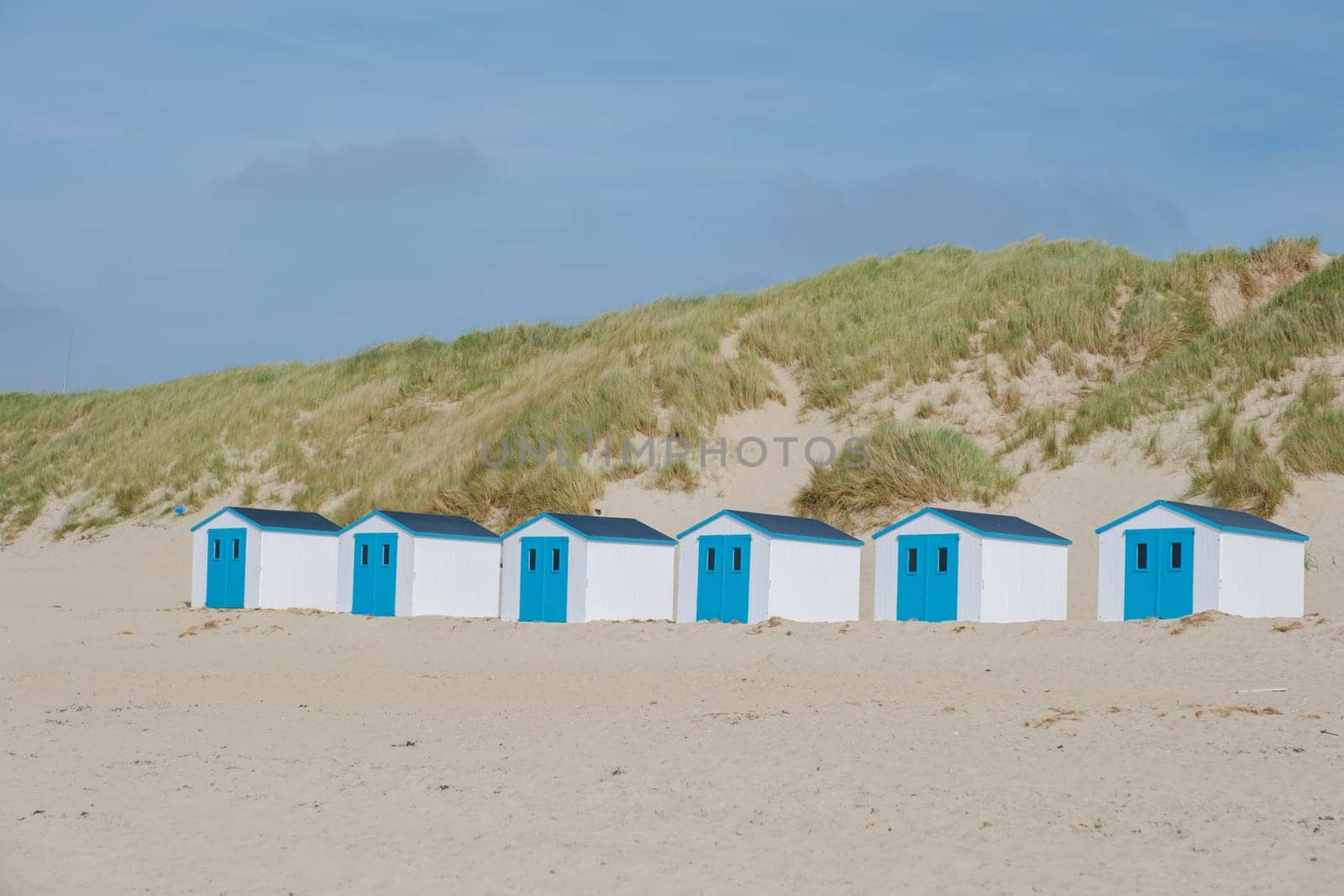 A colorful row of beach huts stands proudly on the sandy shores of Texel, Netherlands, under a clear blue sky. De Koog beach Texel