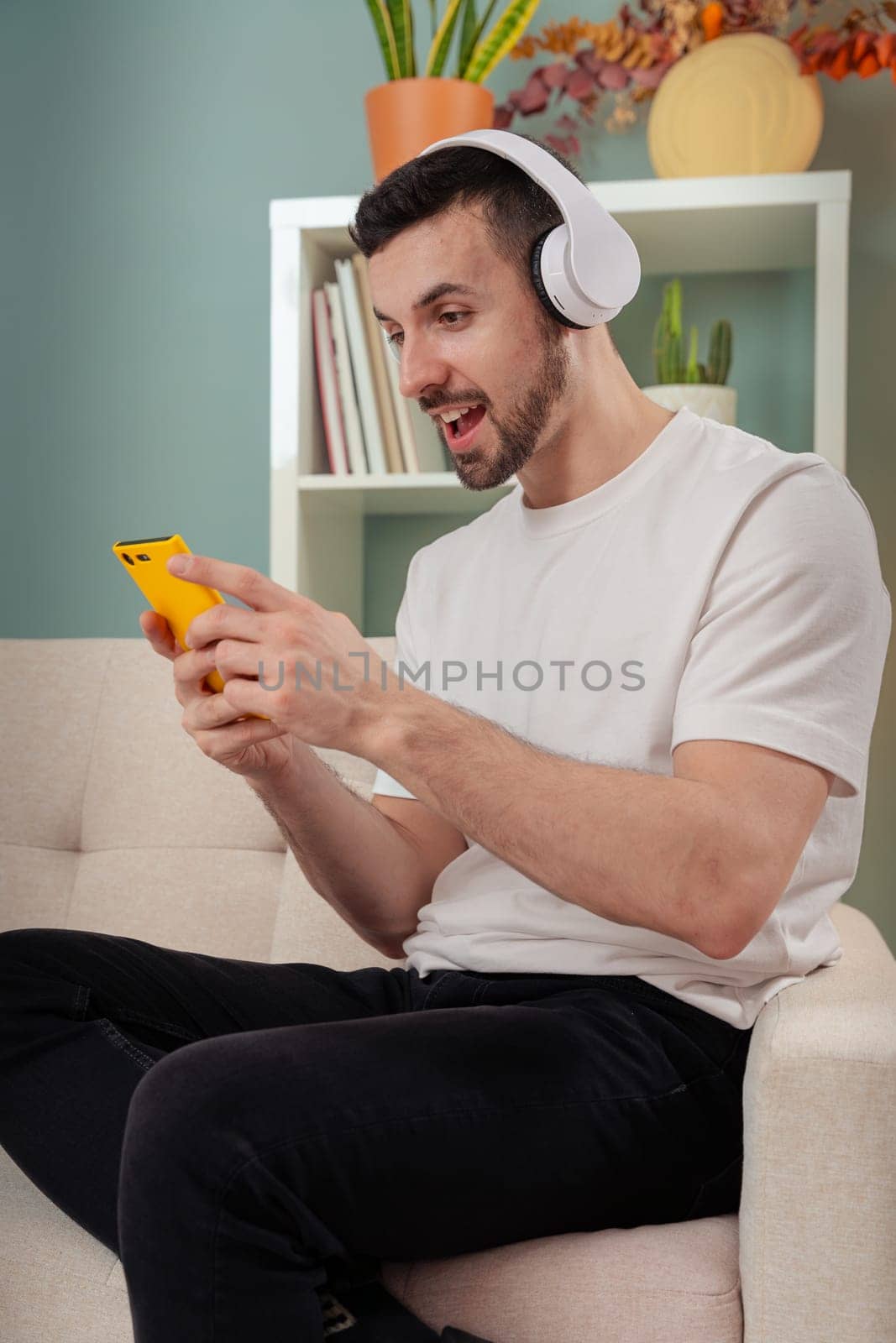 Vertical shot surprised young man sitting on a sofa looking at social media with a smartphone by mariaphoto3