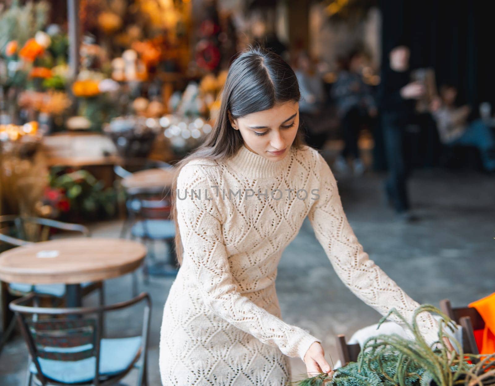 A young woman making a holiday wreath at a Christmas decoration workshop. by teksomolika