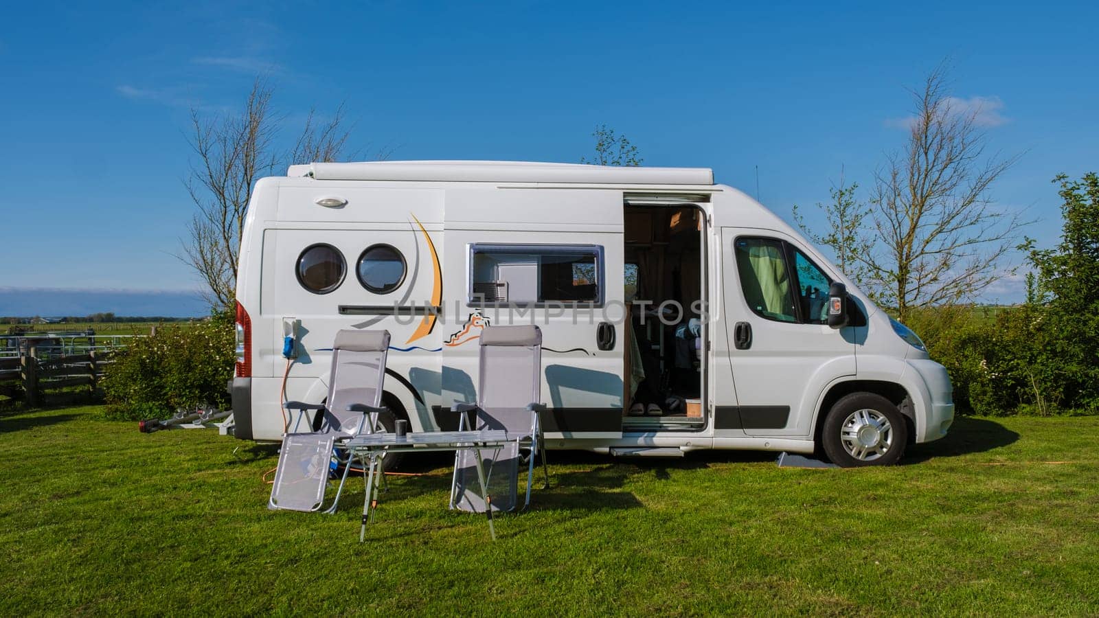 A modern RV is peacefully parked on a lush green field in Texel, Netherlands, surrounded by the beauty of nature under a clear blue sky.