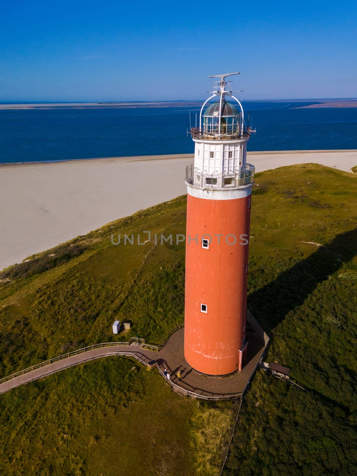 An aerial perspective of a picturesque white lighthouse standing proudly on the sandy shores of Texel, Netherlands, overlooking the vast expanse of the sea.