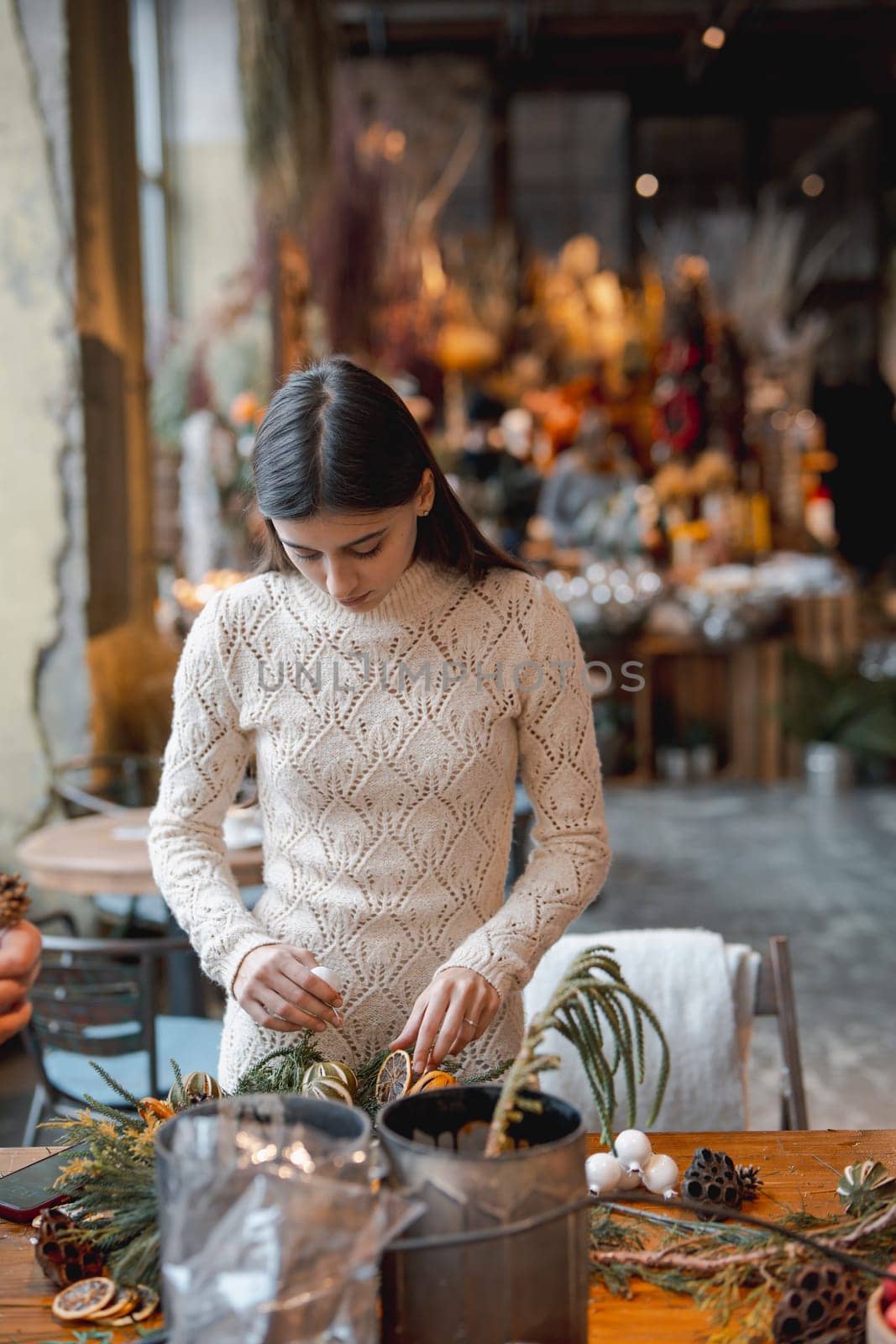 A young woman crafting a Christmas wreath at a holiday decor workshop. by teksomolika