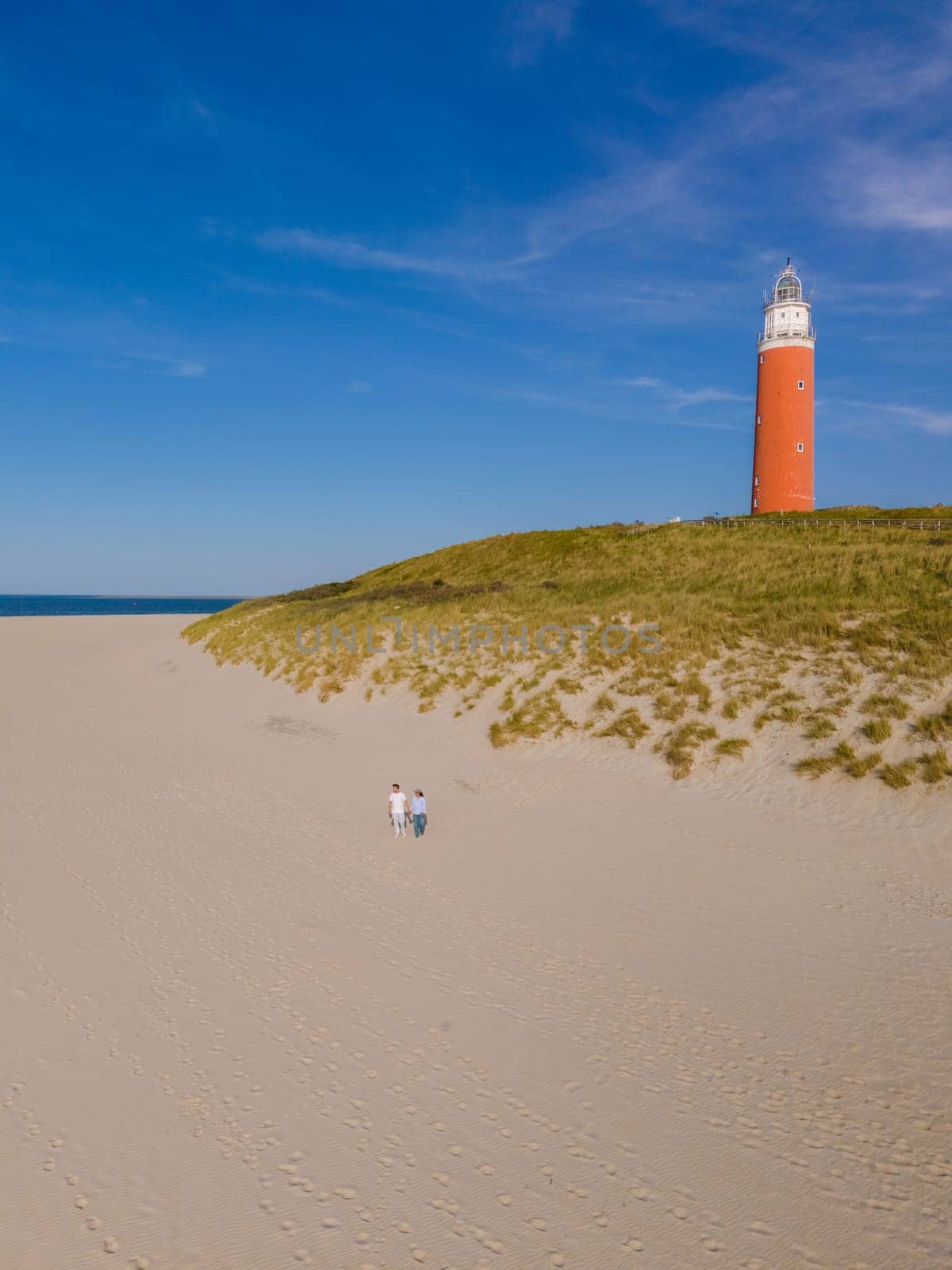 A majestic lighthouse stands tall on a sandy beach, guiding ships safely to shore with its bright beacon of light against the backdrop of the sea.