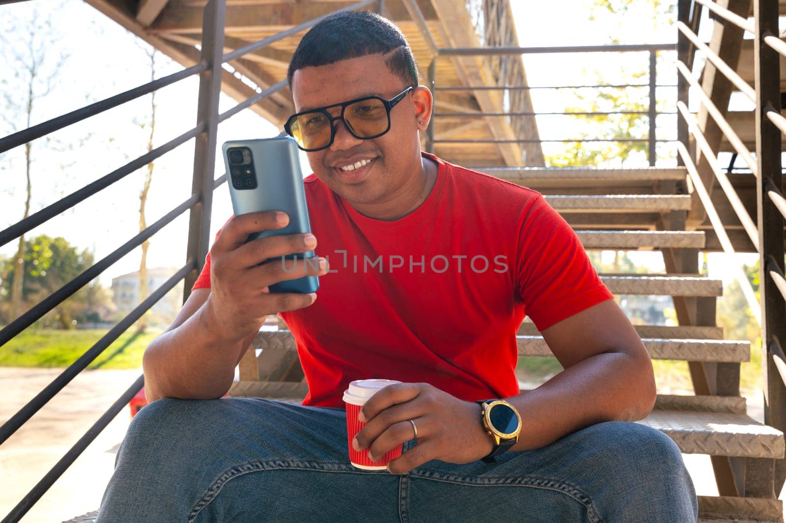 Happy Latin man smiling while browsing the internet with a telephone feeling of happiness outdoors.