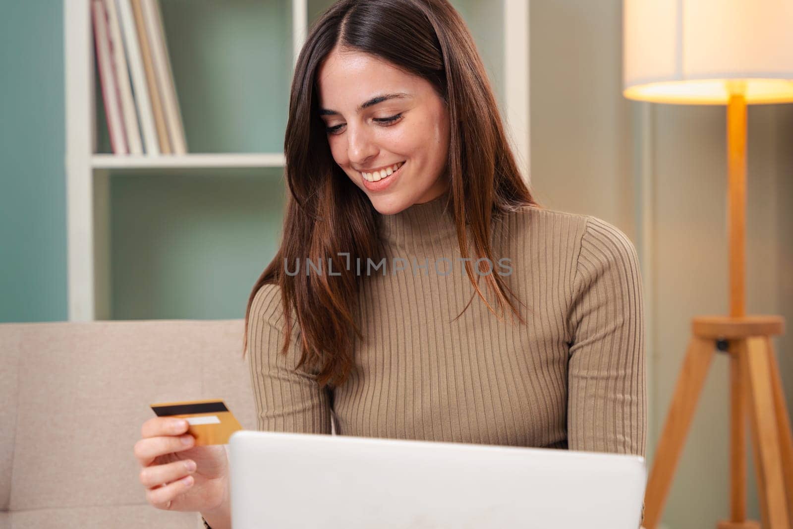 Pretty young caucasian woman shopping online with credit card and laptop while sitting on the couch at home.