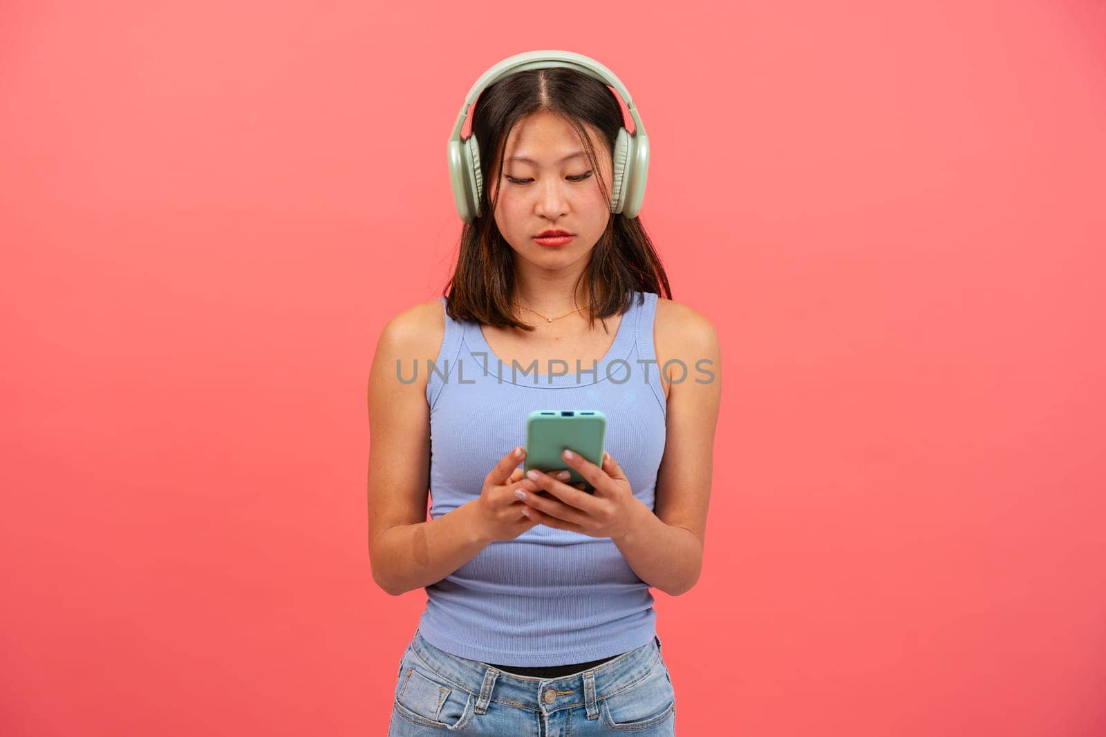 Portrait of angry girl looking at mobile phone, serious, texting on pink background. Concept of human emotions, facial expression. Copy space for your ad