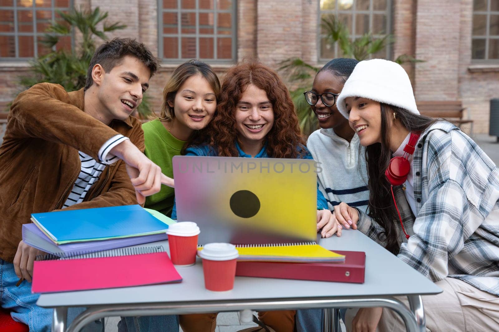 A group multiethnic of five students with a computer and notes sit near campus to review the exam.