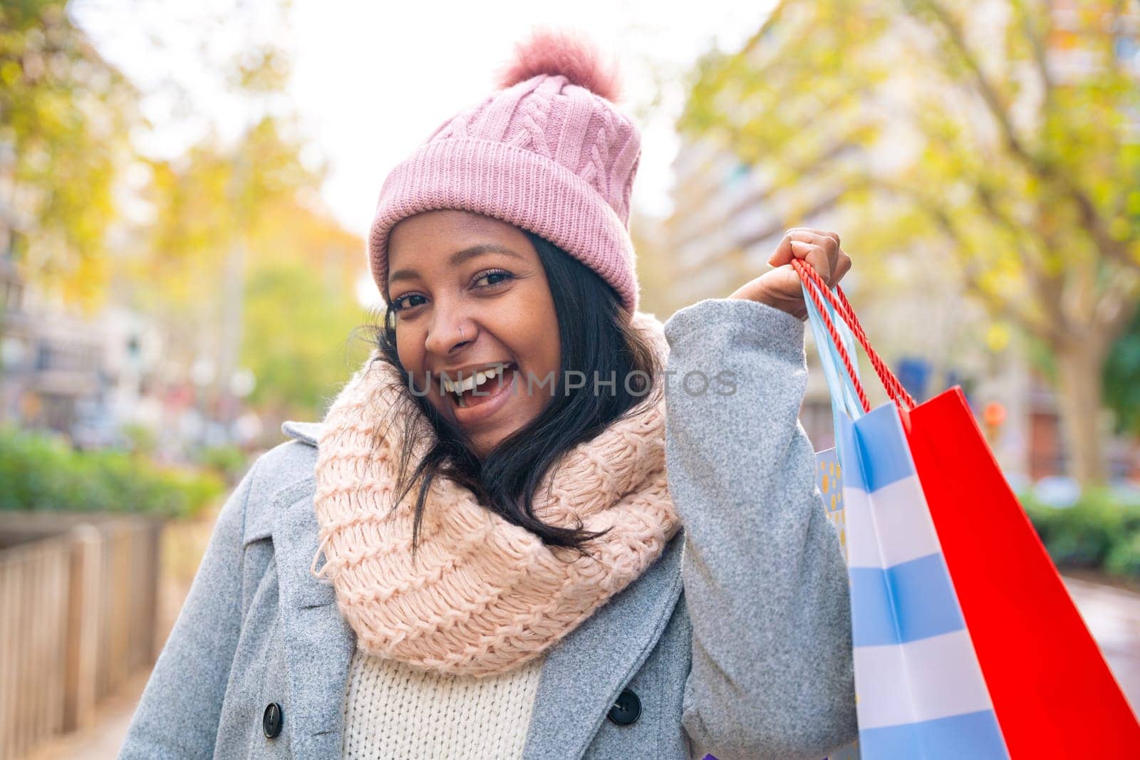 Portrait of a smiling young woman showing shopping bags in hand looking at camera outdoors. by mariaphoto3