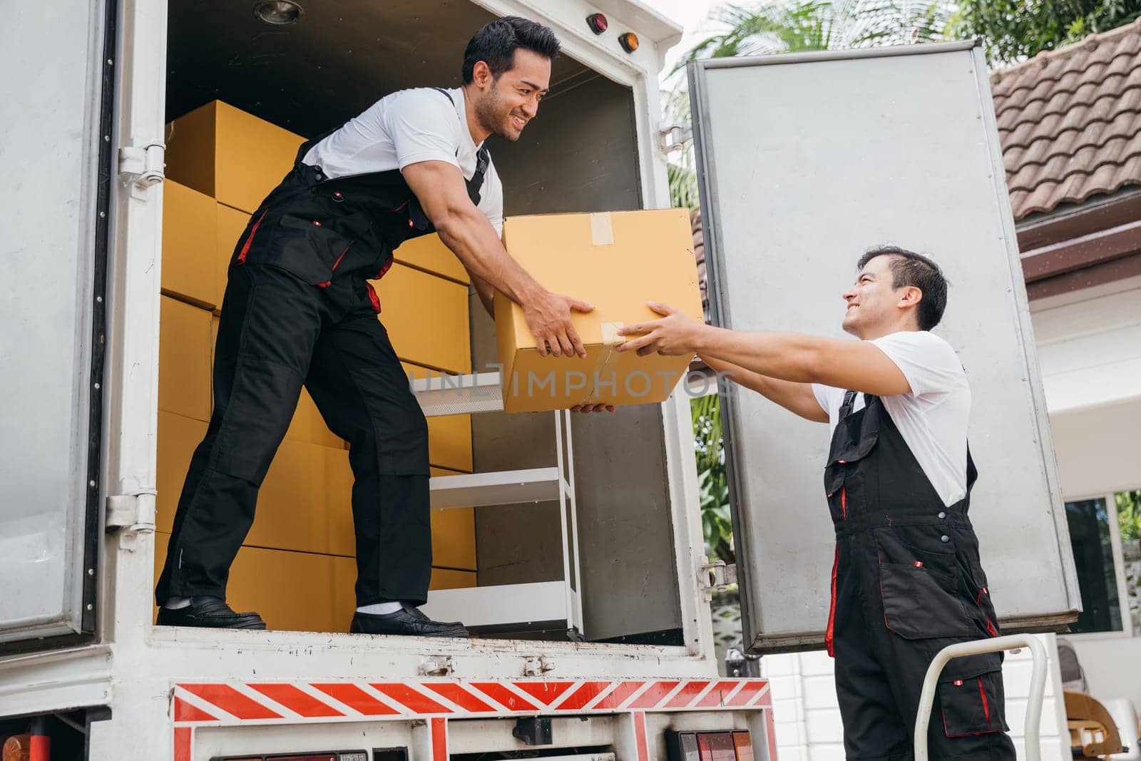 Smiling employees of a removal company work in uniform unloading boxes and furniture from the truck. Their dedication guarantees a smooth delivery into the new home ensuring happiness. Moving Day by Sorapop