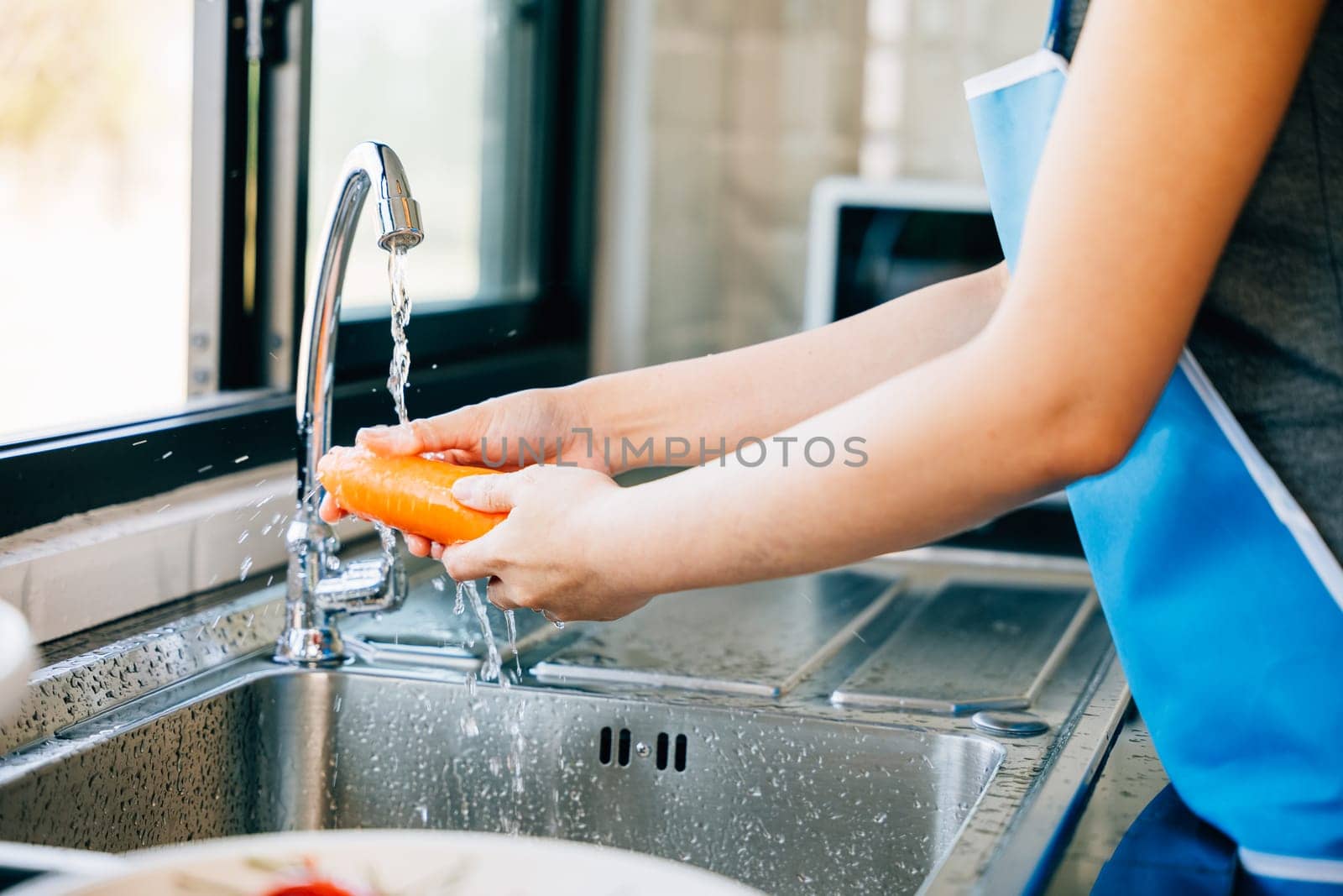 A young woman cleans and washes carrots in the kitchen by Sorapop