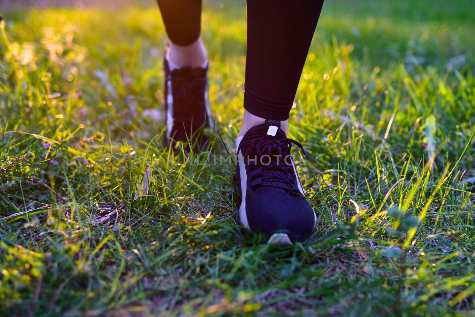 Woman's legs in black leggings and black sneakers on nature background walking on grass