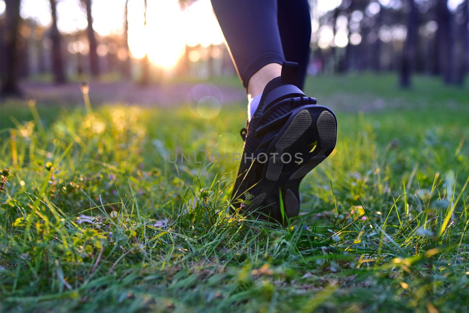 Close up Woman's legs in black sneakers walking on grass, back view.