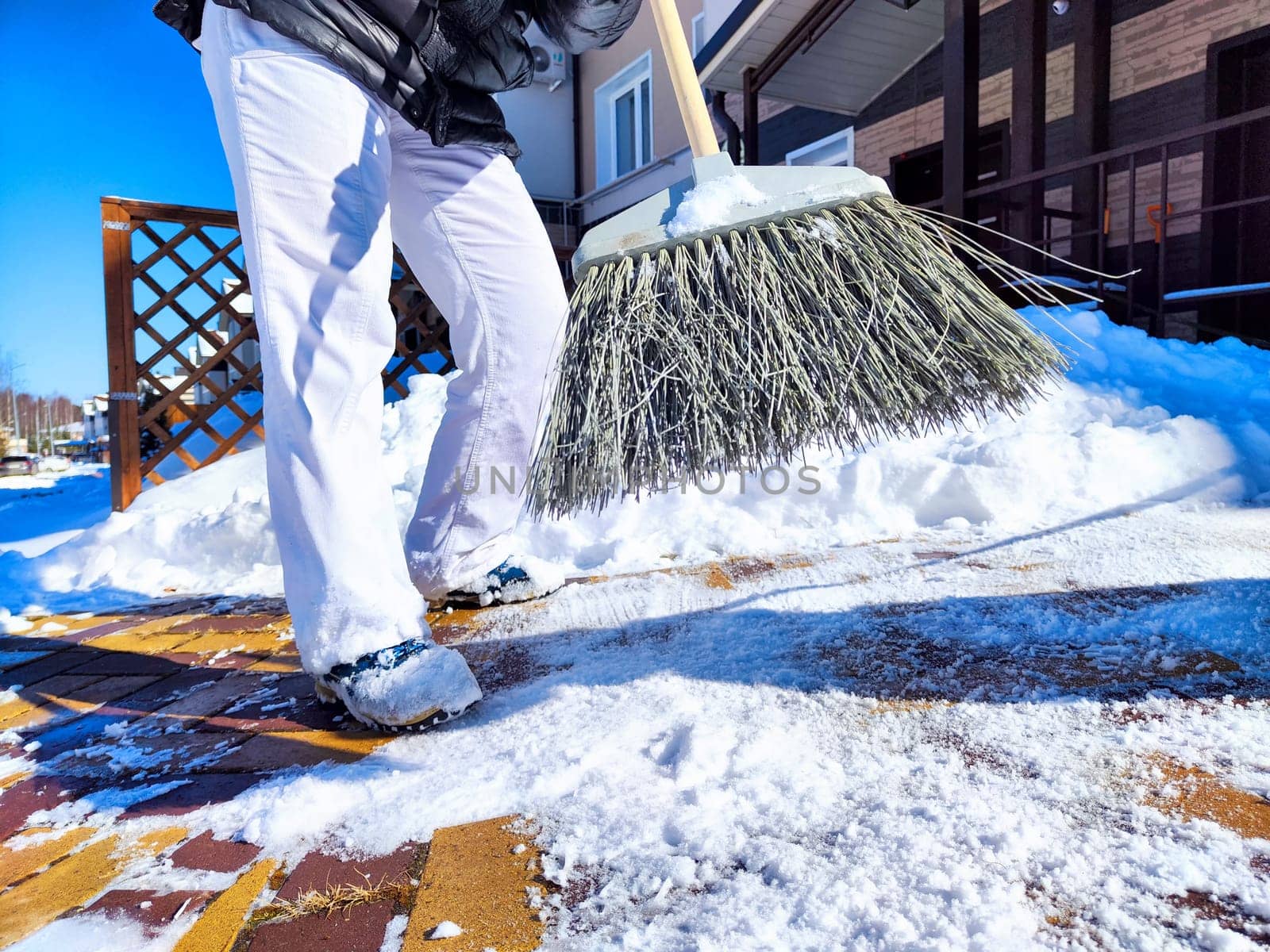 Clearing Snow From Sunny Yard With Broom. Person sweeps fresh snow off the brick path in front of house