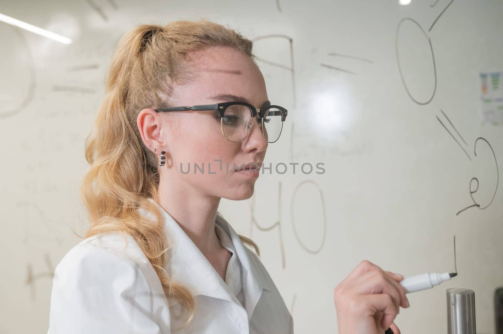 A Caucasian woman in a medical gown thinks and finalizes formulas on a transparent wall