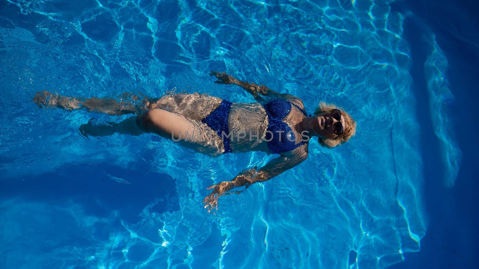 An elderly woman in sunglasses swims on her back in the pool. Vacation in retirement