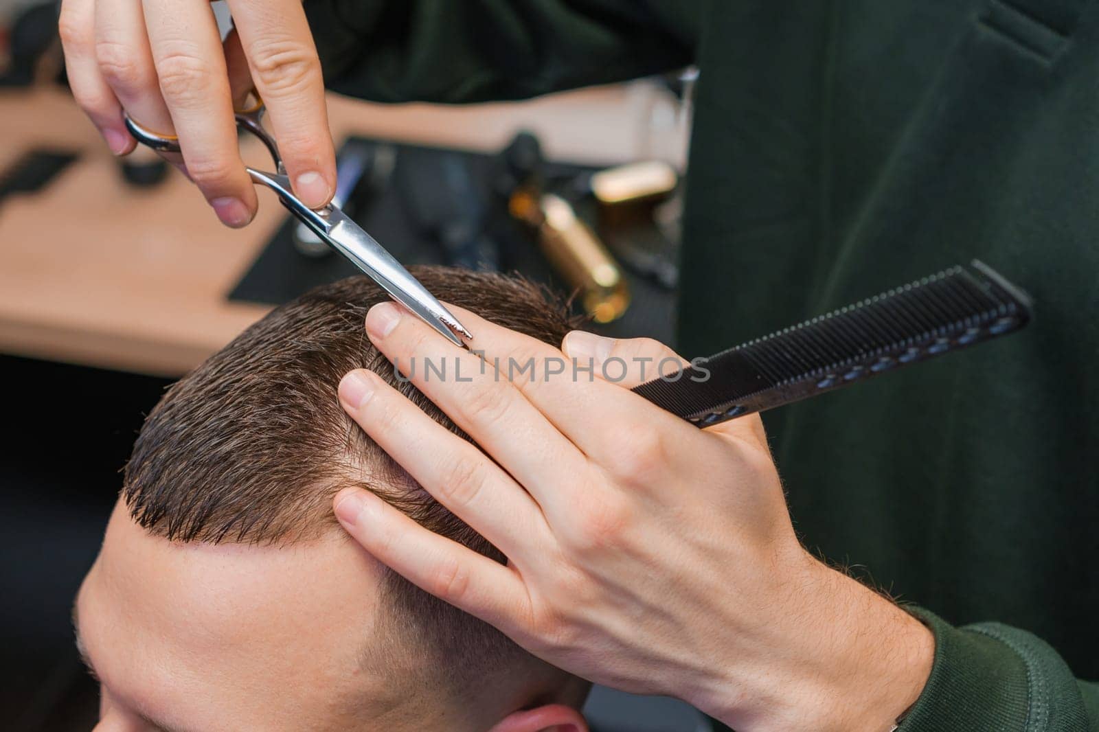 Hairstylist expertly trims the clients brunette hair using scissors at the barbershop