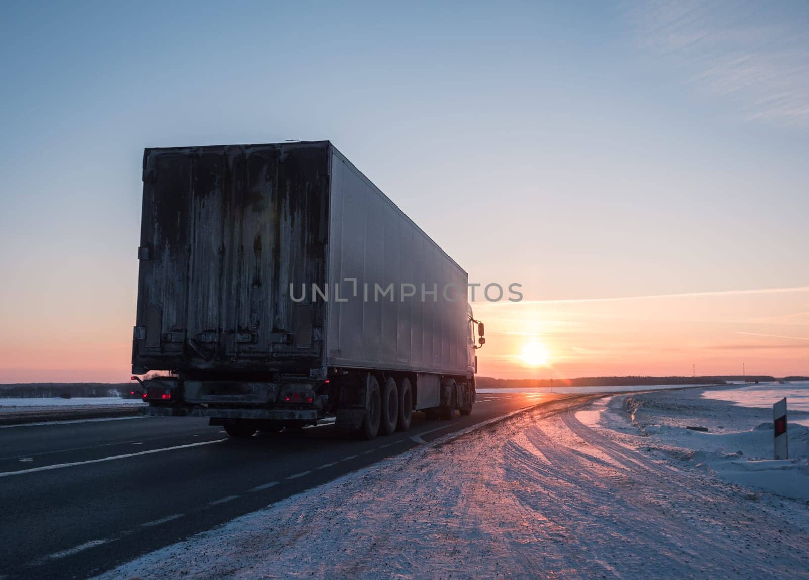 Semi truck driving along a snowy highway at sunset in winter by Busker