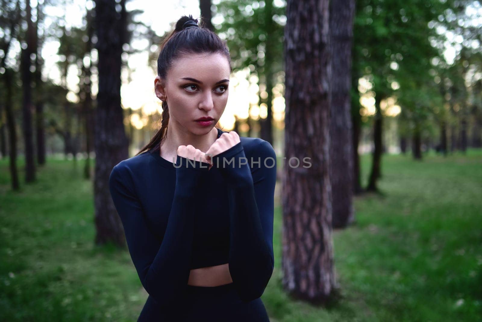 sporty woman doing martial arts training in sporty black top holding hands in fighting pose against forest background.