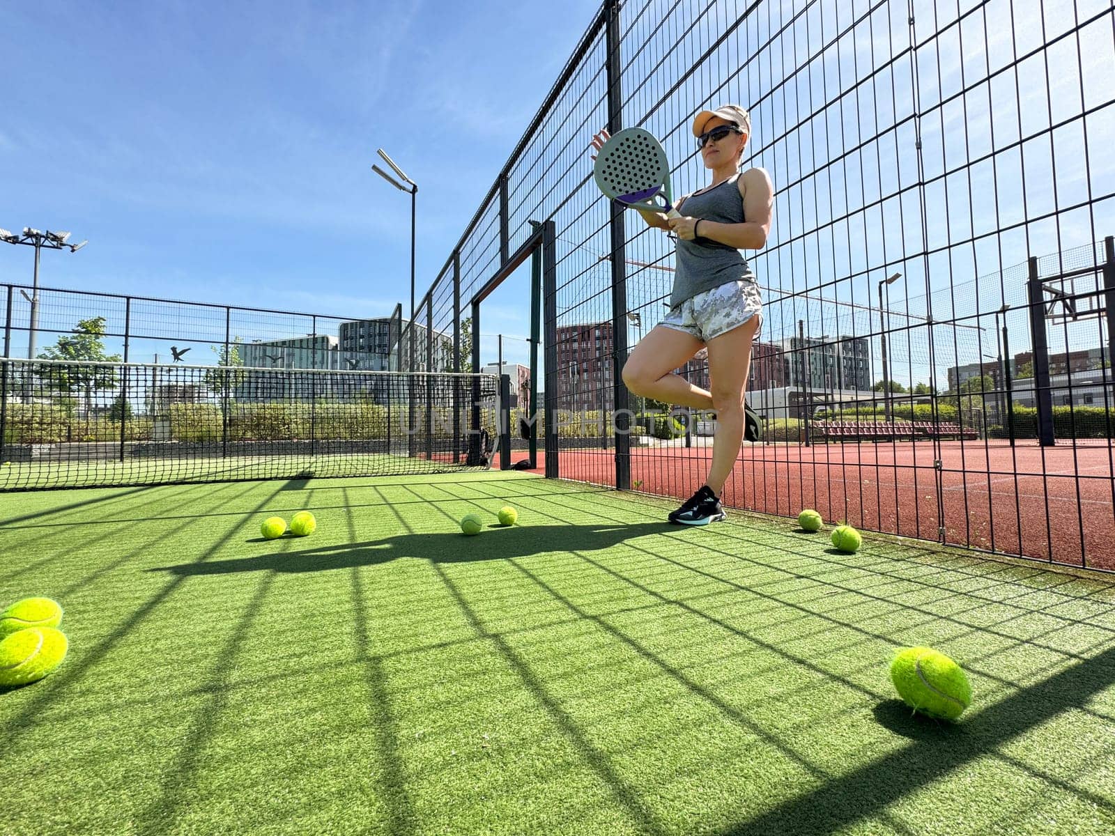 Portrait of active emotional woman playing padel tennis on open court in summer, swinging racket to return ball over net .. High quality photo