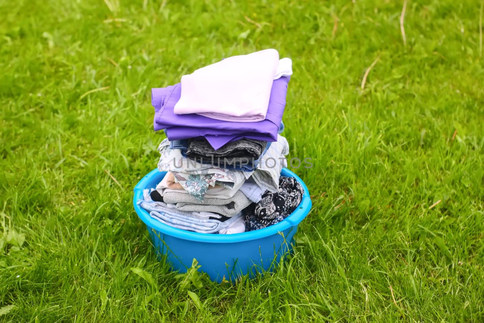 Colorful washed dry clothes in plastic bowl on the green grass background.