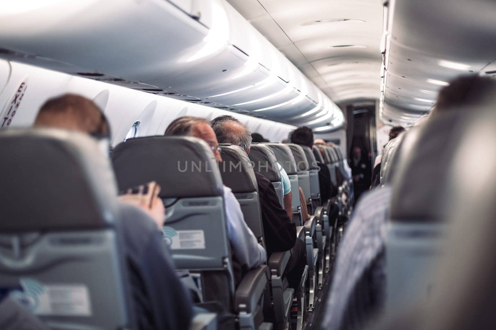 Interior of airplane with passengers on seats and stewardess in uniform walking the aisle, serving people. Commercial economy flight service concept