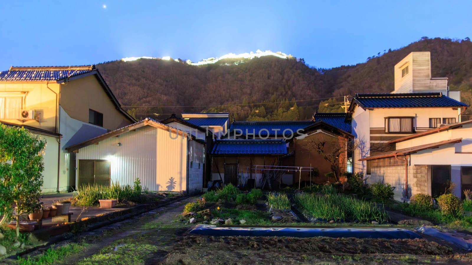 Small garden by houses in quiet neighborhood with lights from Takeda Castle at night. High quality photo