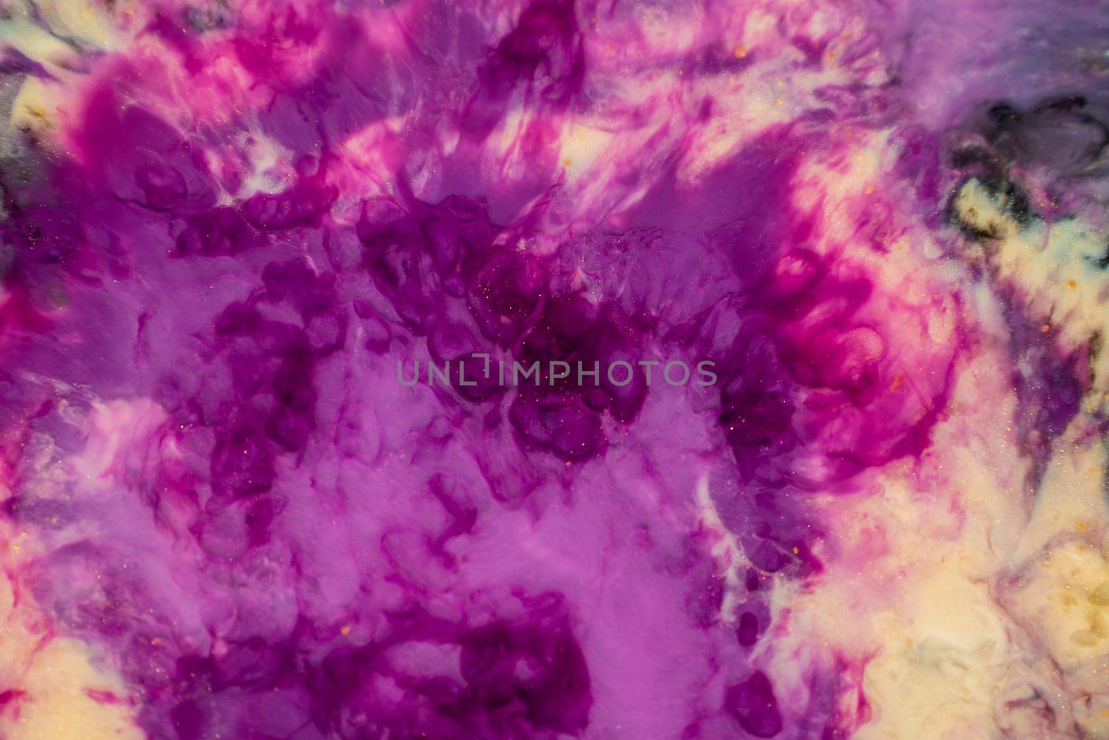 A close up of purple and yellow ink swirling in water, creating a vibrant art piece reminiscent of petals on a violet or magenta plant