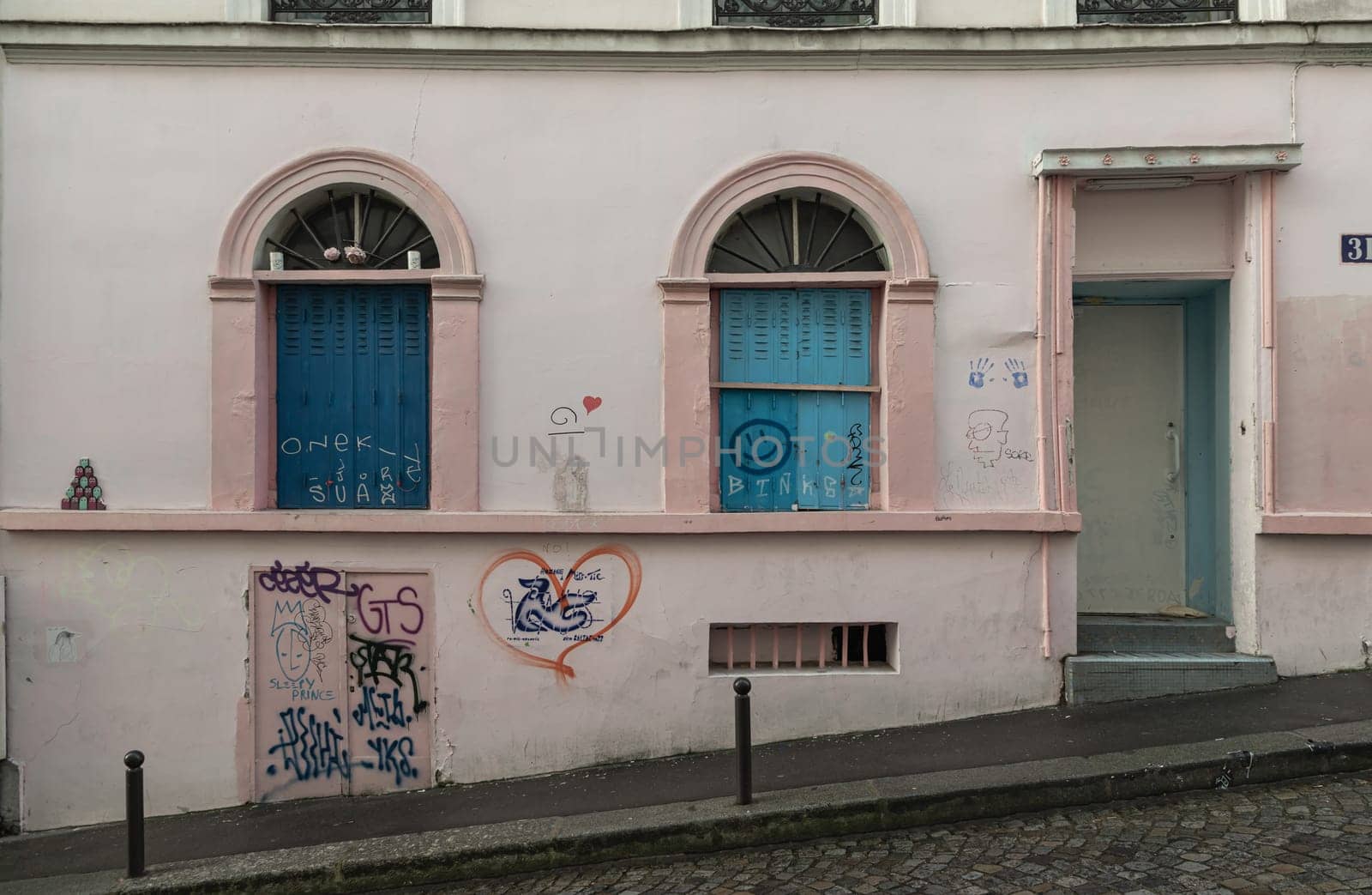 France, Paris - Jan 03, 2024 - View of blue windows and doorway on old wall of a ground floor residence on montmartre streets in Paris. A narrow cobblestone street with typical French architecture descends and rises, The historic district of Montmartre in the city of Paris, Space for text, Selective focus.