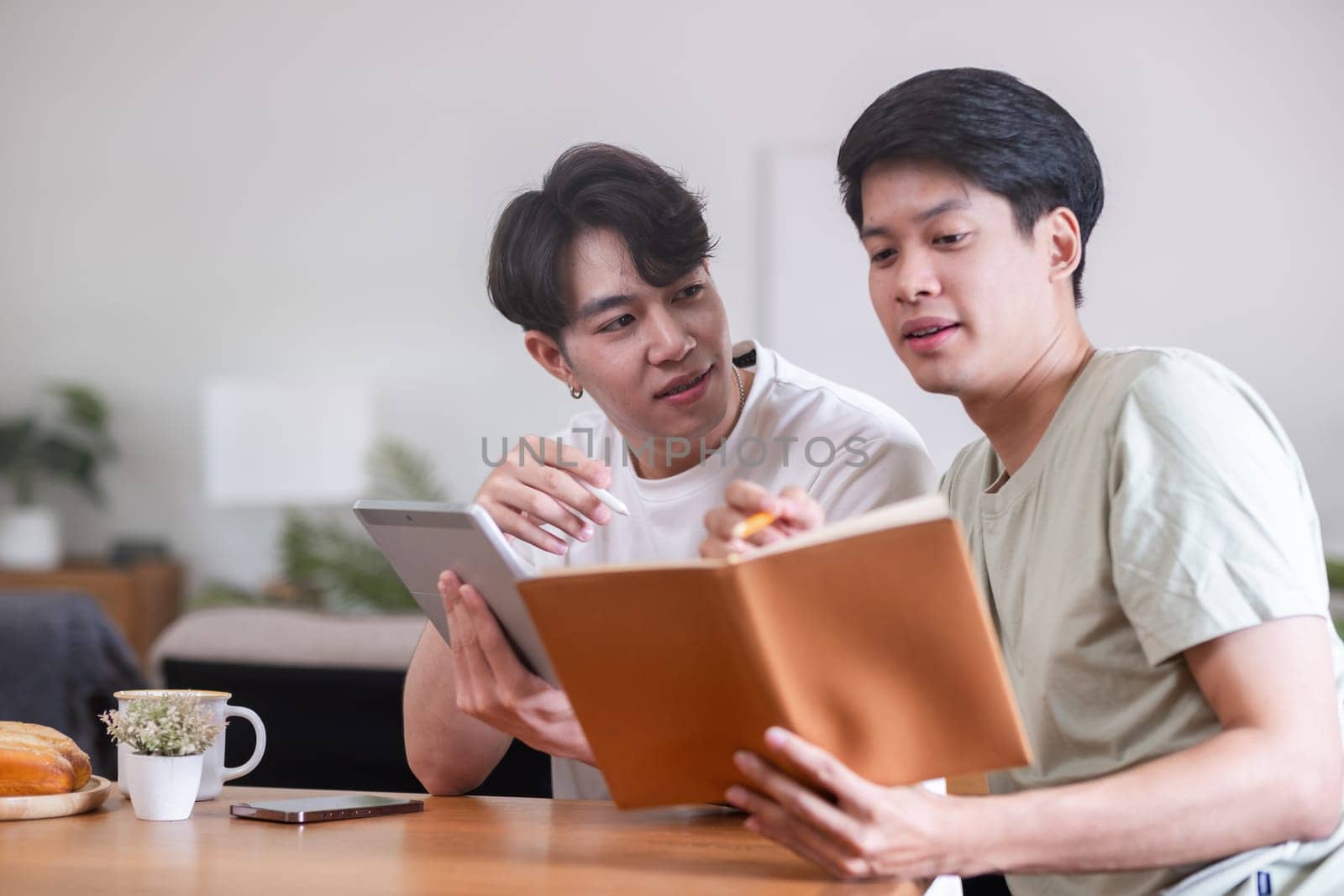 A male lgbt couple is studying together while studying online at home to prepare for an online exam. by wichayada