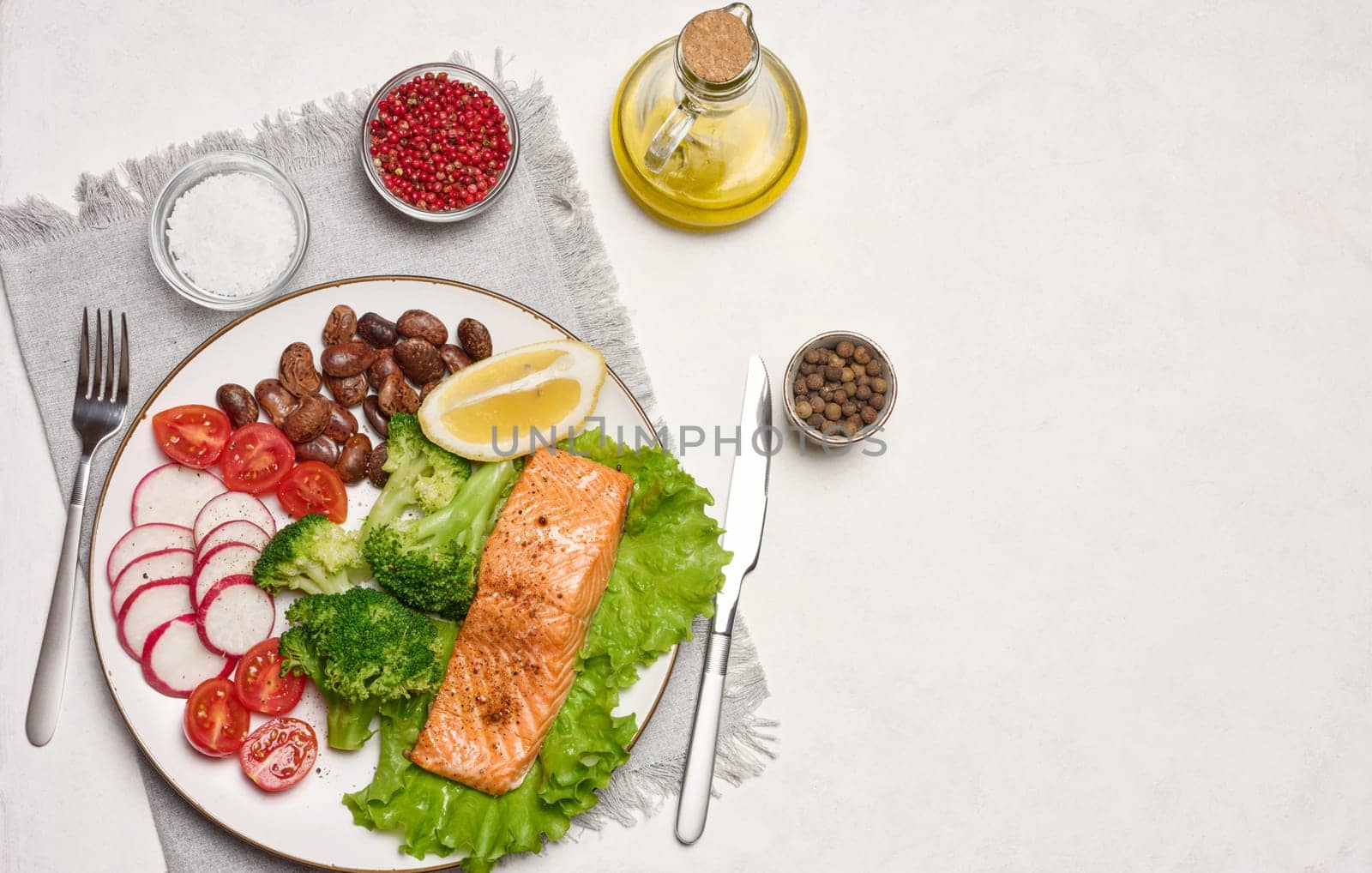 Healthy lunch with grilled salmon on green lettuce, next to vegetables, tomatoes, radishes, broccoli and a portion of beans.