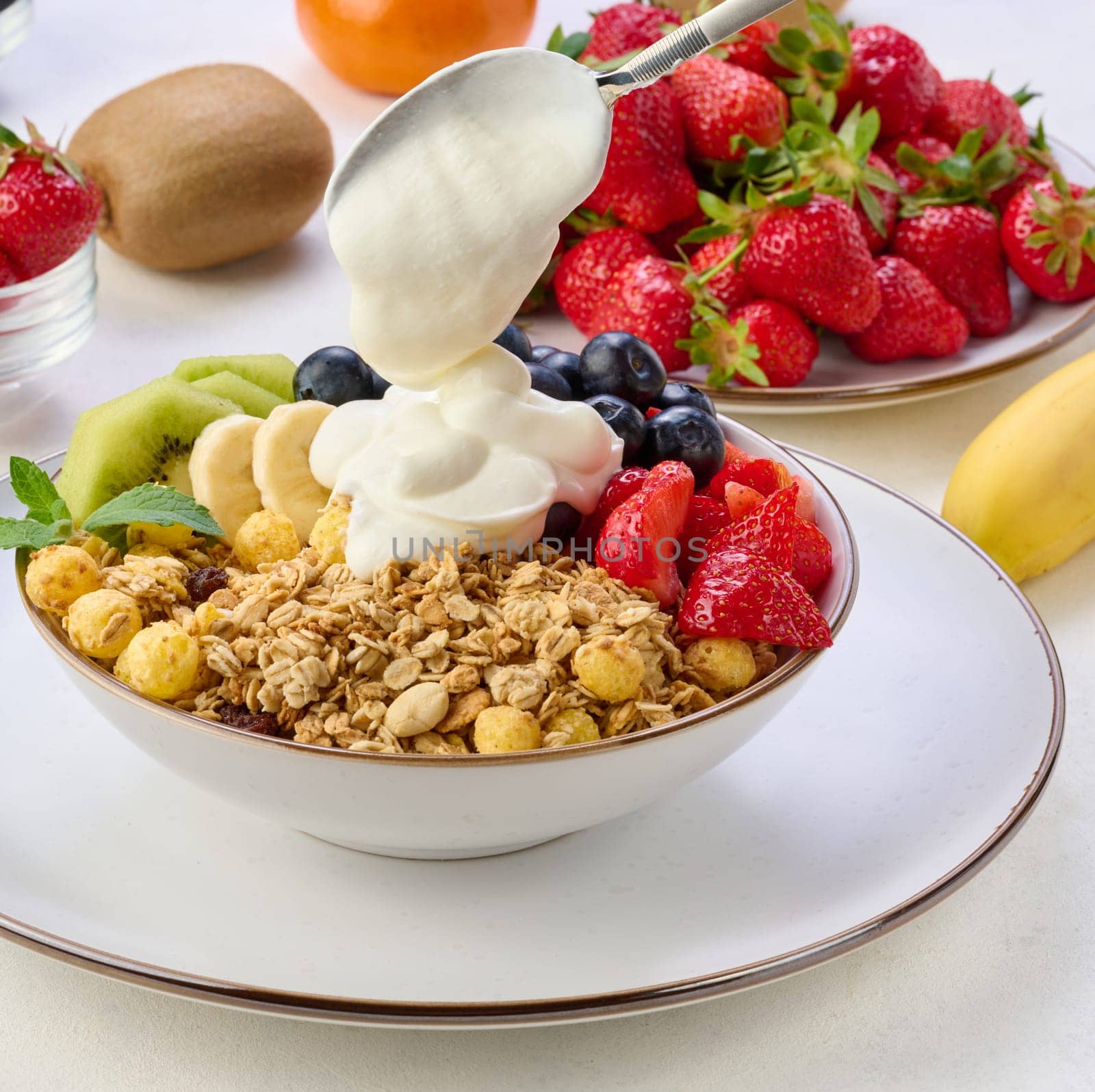 Granola with strawberries, kiwi, banana and blueberries in a round plate on a white table. Healthy and tasty food by ndanko