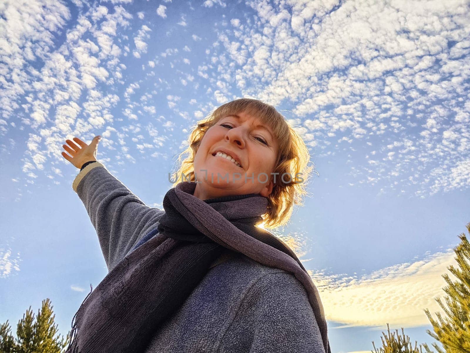 Happy female blonde tourist taking selfie picture with smart mobile phone outside. Middle aged woman having fun on adventure trip and blue sky on background